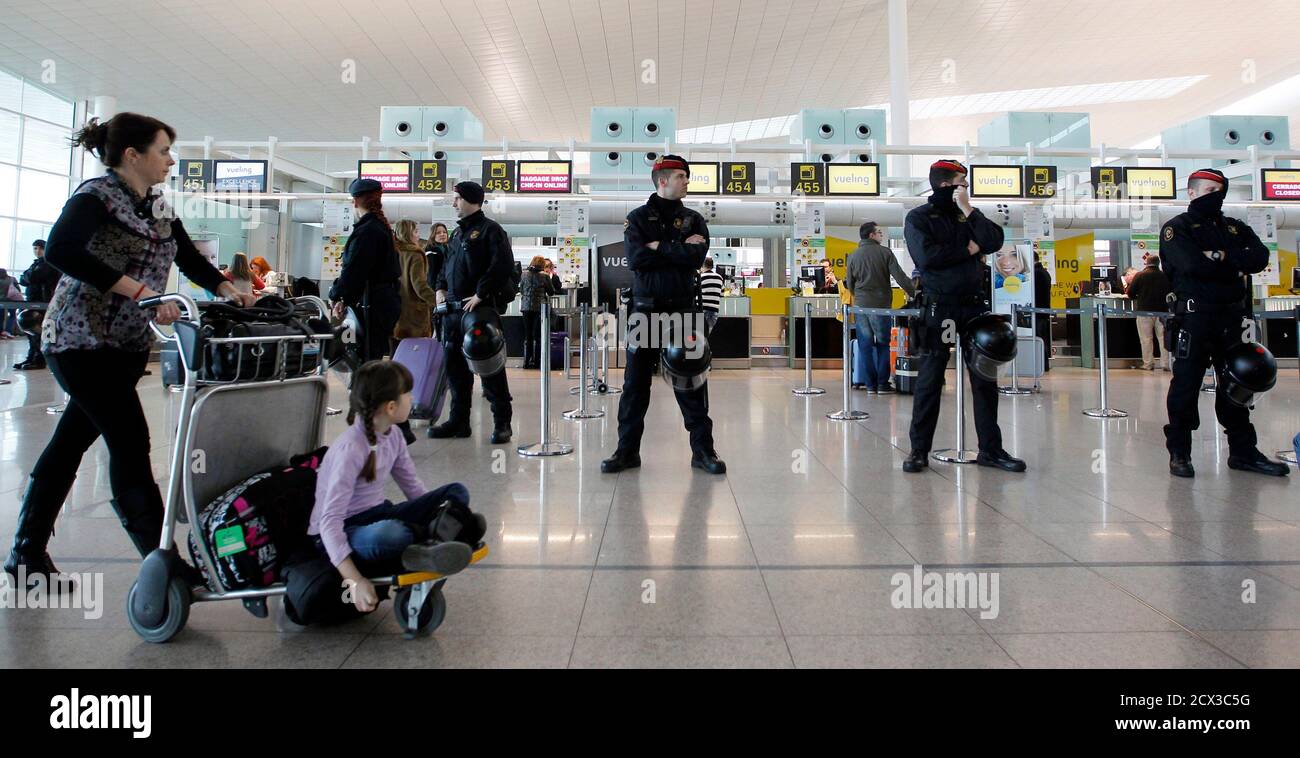 Riot police officers stand guard at a Vueling check-in desk as passengers  walk past during a protest by Iberia workers at Terminal 1 of Barcelona's  airport, February 18, 2013. Dozens of Iberia