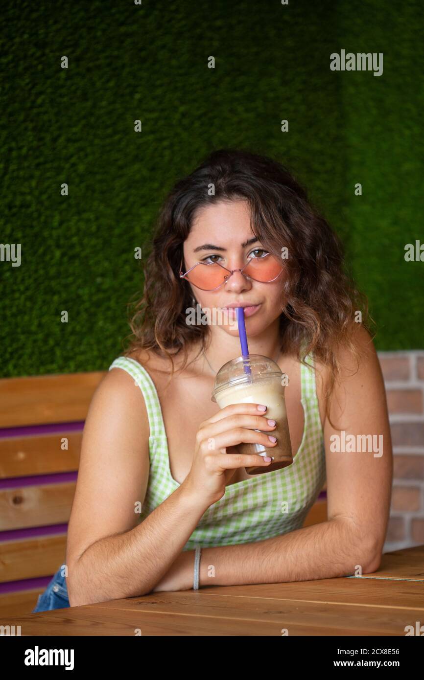 Jeune fille regardant l'appareil photo tout en buvant un smoothie. Banque D'Images