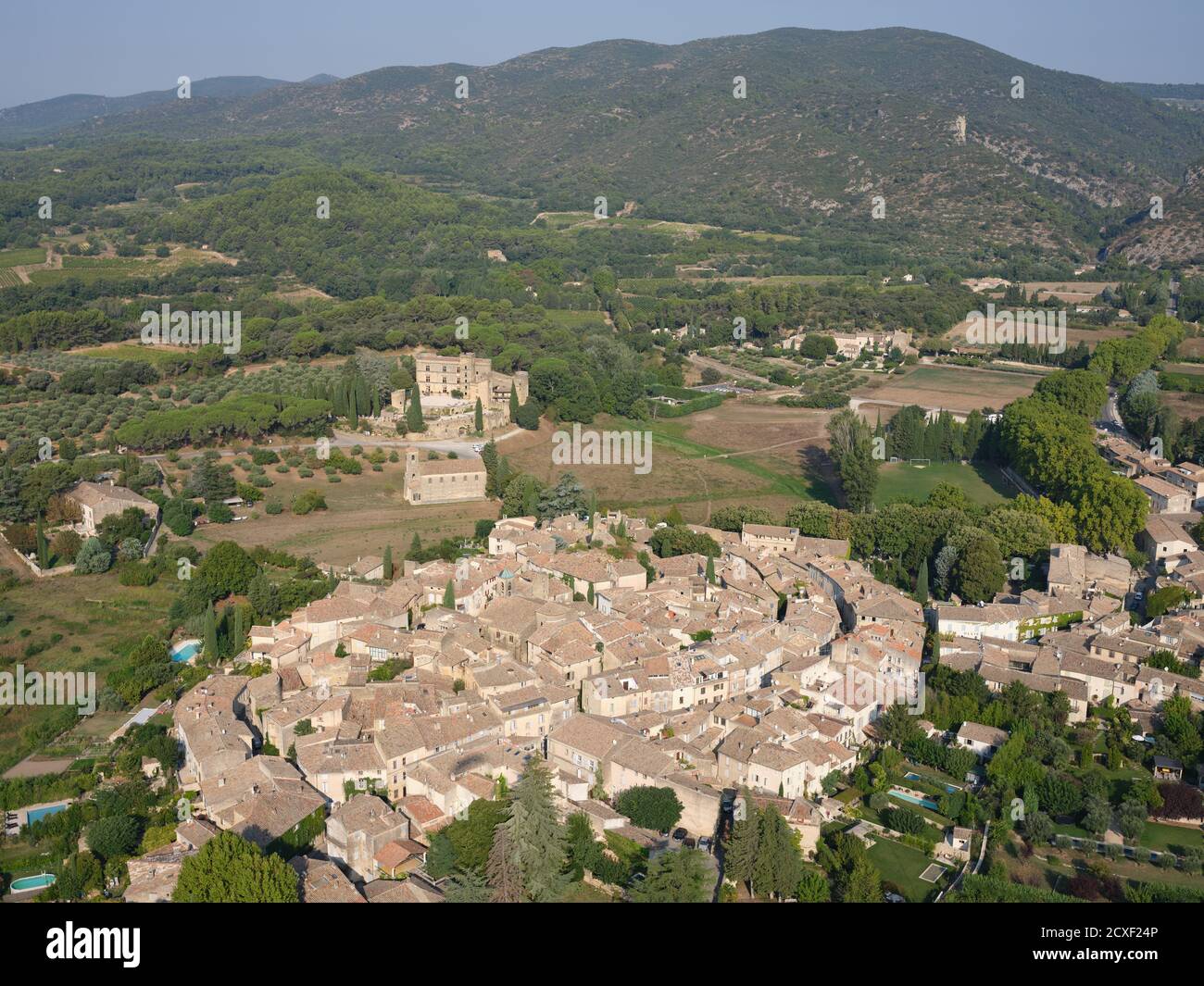 VUE AÉRIENNE.Village médiéval avec son château à l'écart du village, et la montagne du Lubéron au loin.Lourmarin, Vaucluse, France. Banque D'Images