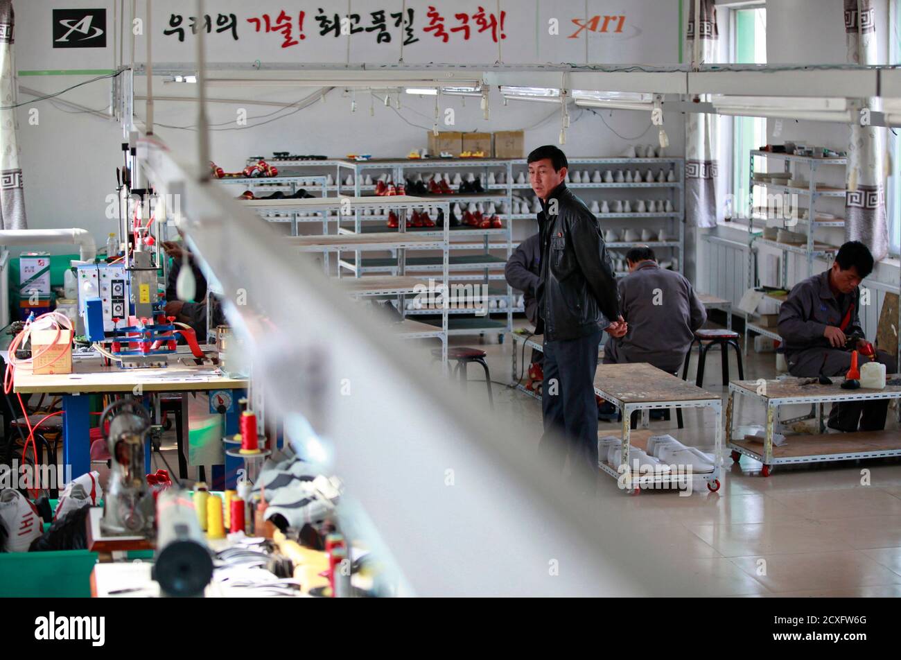 A North Korean manager stands supervising amidst North Korean workers at a  temporary soccer shoe factory in a rural village on the edge of Dandong  October 24, 2012. Top soccer-boot maker Adidas