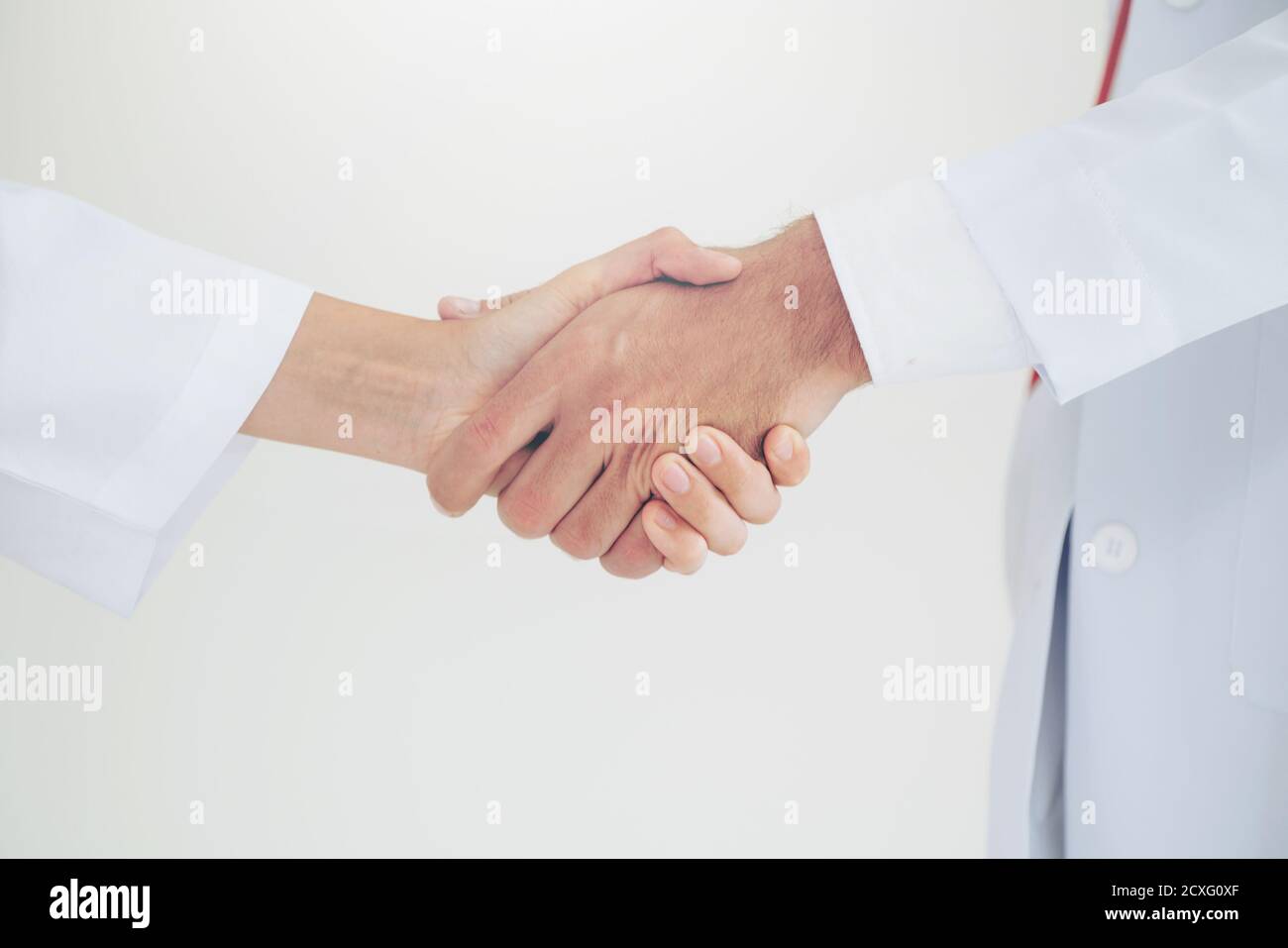 Médecin sur fond blanc donnant la poignée de main à un autre médecin montrant le succès et le travail d'équipe des professionnels de la santé. Gros plan sur les médecins Banque D'Images