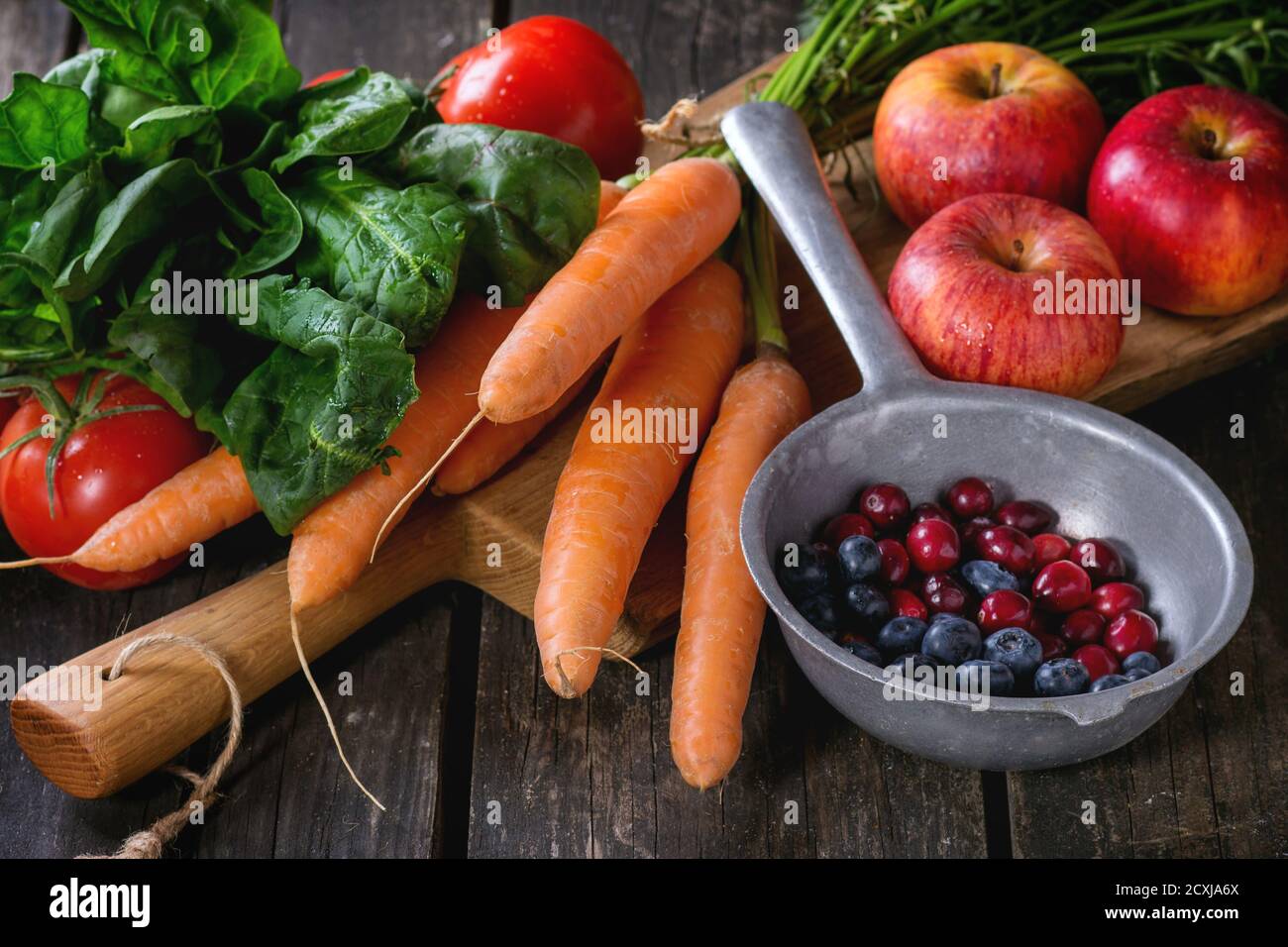 Choix de fruits frais, de légumes et de baies. Botte de carottes, épinards, tomates et pommes rouges sur planche, les bleuets et les canneberges Banque D'Images