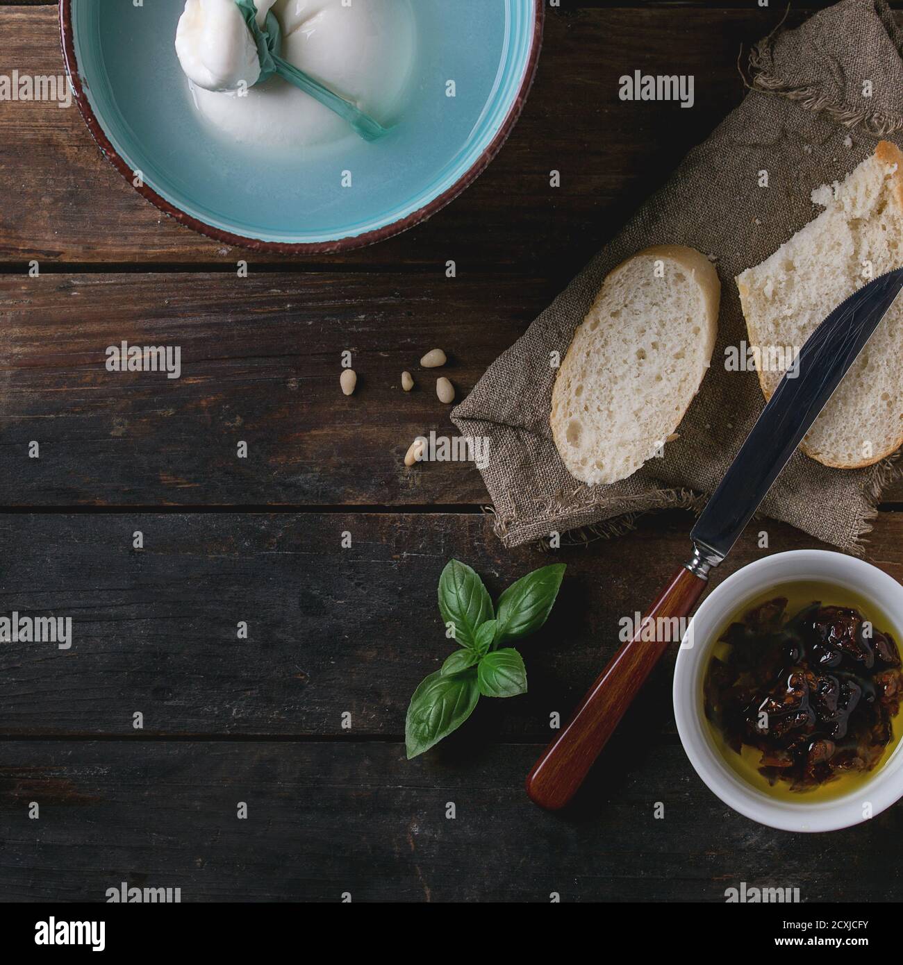 Bol Turquoise ensemble lié à la saumure de burrata fromage italien servi avec des pignons, des tranches de pain, basilic et tomates séchées dans l'huile d'olive avec chiffon et knif Banque D'Images
