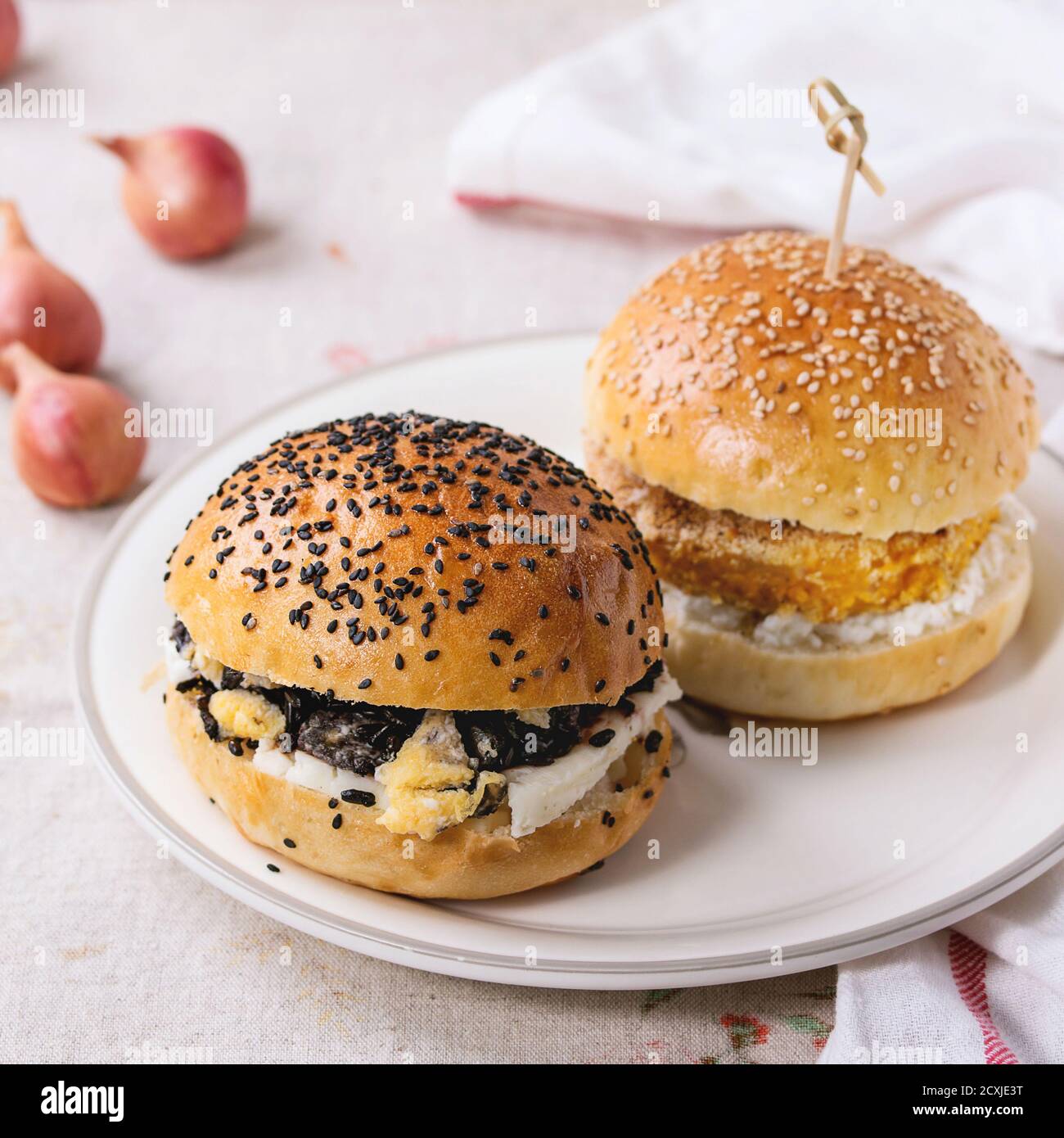 Deux hamburgers végétariens faits maison avec patate douce et riz noir, servis sur une assiette blanche avec une serviette de cuisine sur fond blanc texturé. Image carrée Banque D'Images