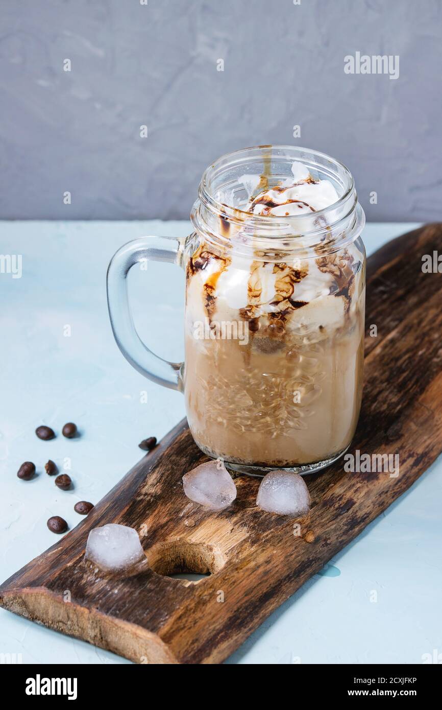 Pot mason de verre avec de la glace café avec crème fouettée, crème glacée et sauce au chocolat, servi avec des grains de café et des cubes de glace sur la planche à découper en bois ove Banque D'Images