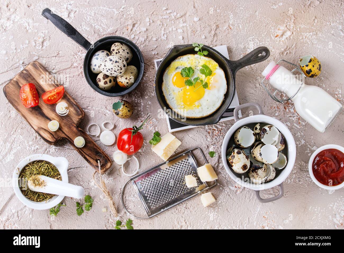 Petit-déjeuner avec des oeufs de cailles dans carter en fonte de fer, tomates cerises, oignons, sauce ketchup, les assaisonnements dans le mortier, râpe à fromage, la coquille en pot. Beige Banque D'Images