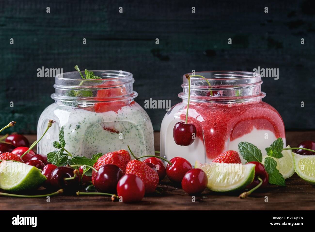 Deux pots en verre carrés avec yaourt maison à la menthe, purée de fraises, graines de cerise et de chia servies avec des baies fraîches et de la lime tranchée sur du woo sombre Banque D'Images