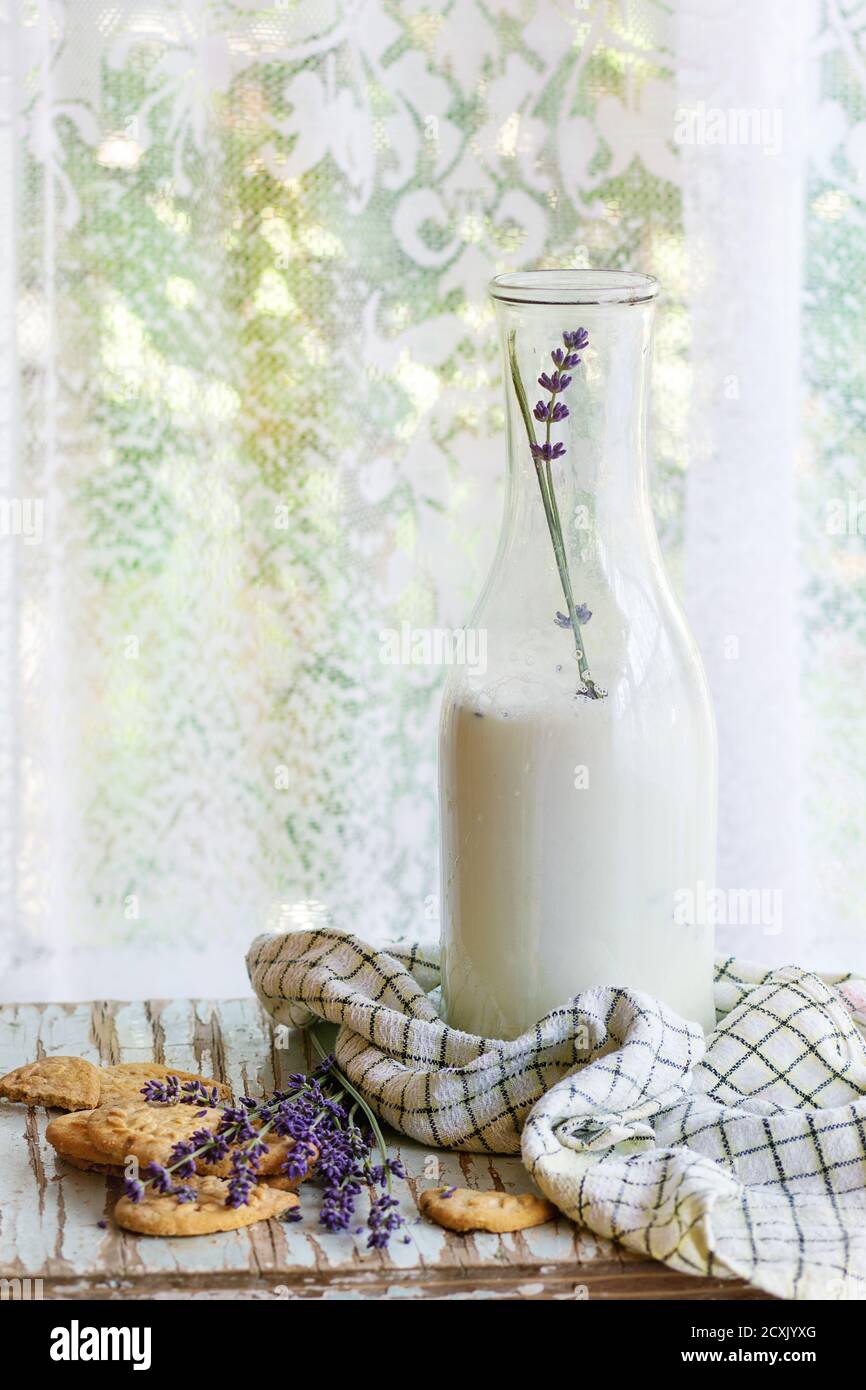 Biscuits à la lavande et bouteille de lait aromatique, servis avec une serviette de cuisine sur une table en bois avec fenêtre à l'arrière-plan. Petit déjeuner de style rustique, natu Banque D'Images