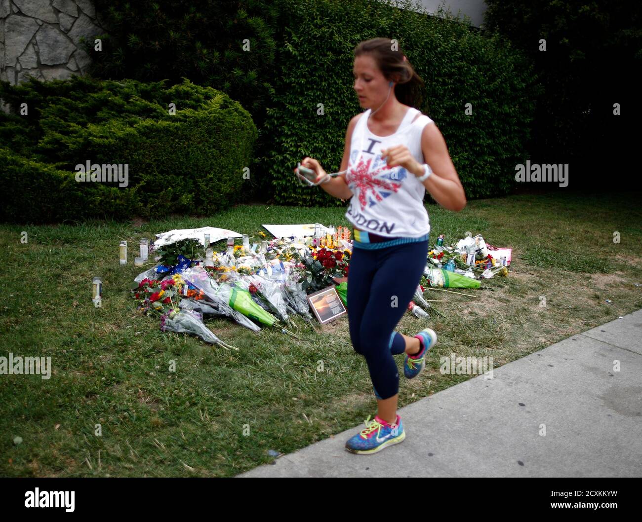 A woman jogs past a makeshift memorial in front of the Alpha Phi sorority house where two women were killed in the Isla Vista neighborhood of Santa Barbara, California May 26, 2014. Twenty-two year old Elliot Rodger killed six people before taking his own life in a rampage through a California college town shortly after he posted a threatening video railing against women, police said on Saturday.  REUTERS/Lucy Nicholson   (UNITED STATES - Tags: CRIME LAW) Banque D'Images