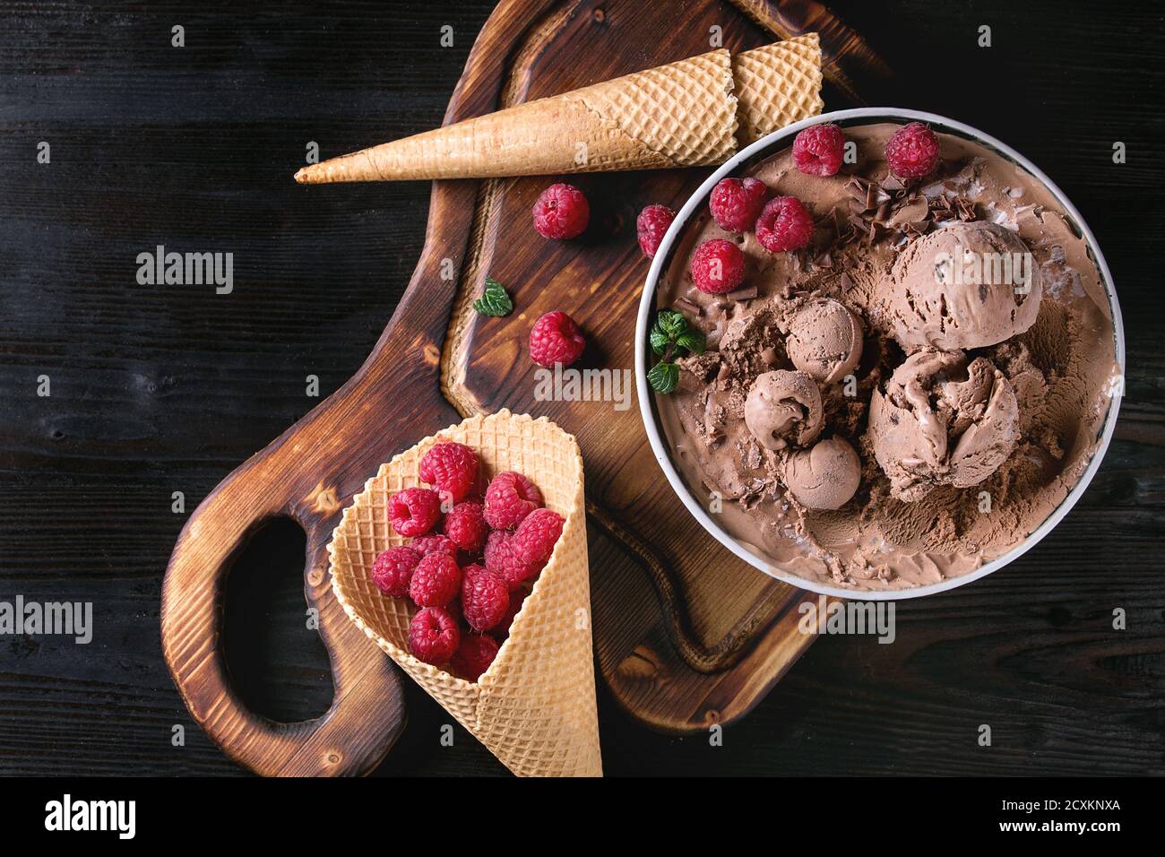 Bol de glace au chocolat fait maison avec les framboises, menthe et cornet gaufré sur bois servant au fond de bois brûlé noir. Vue supérieure w Banque D'Images