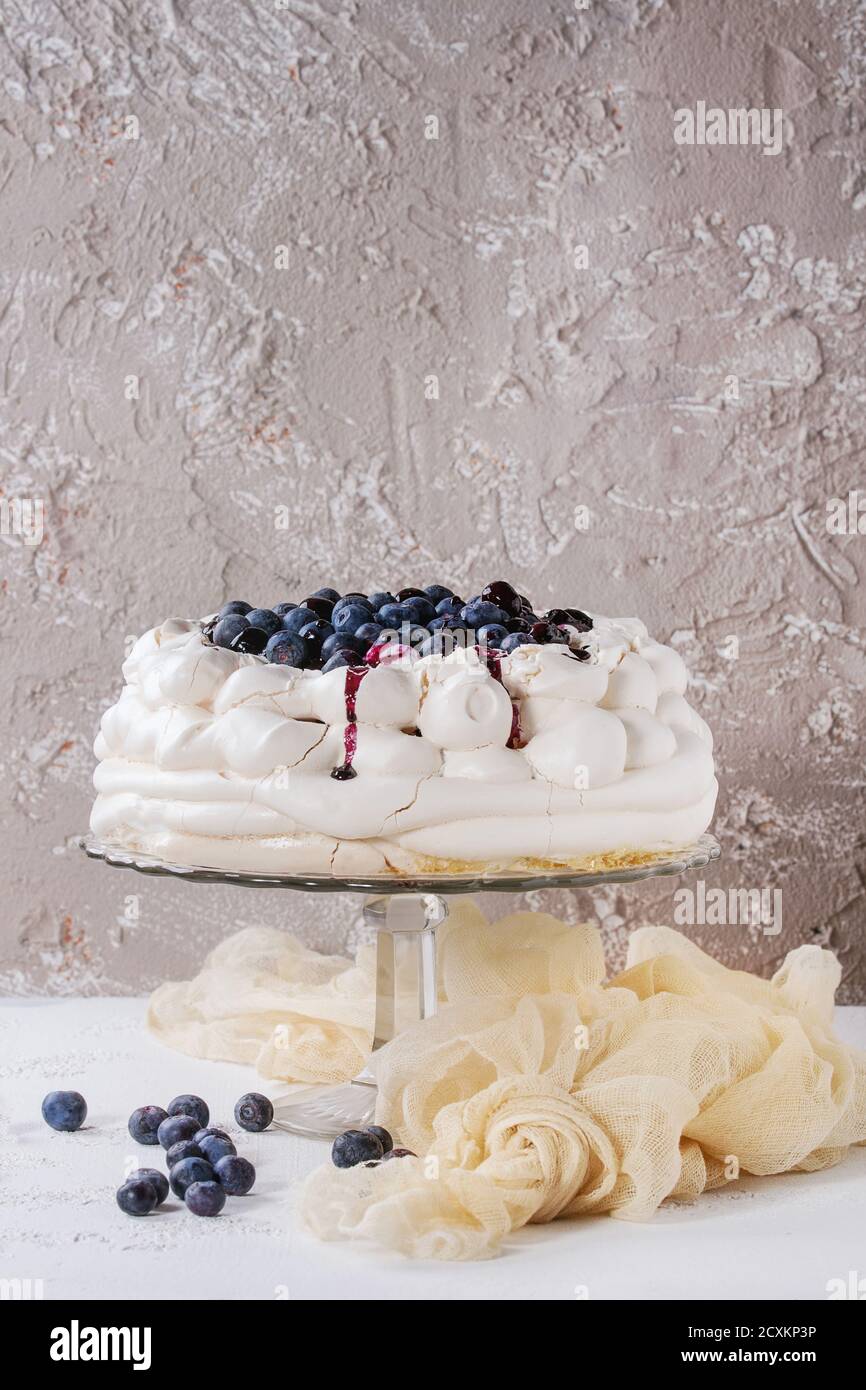 La meringue maison Pavlova gâteau de crème fouettée, de bleuets frais et sauce aux bleuets sur cake stand vintage beige sur fond texture béton, g Banque D'Images