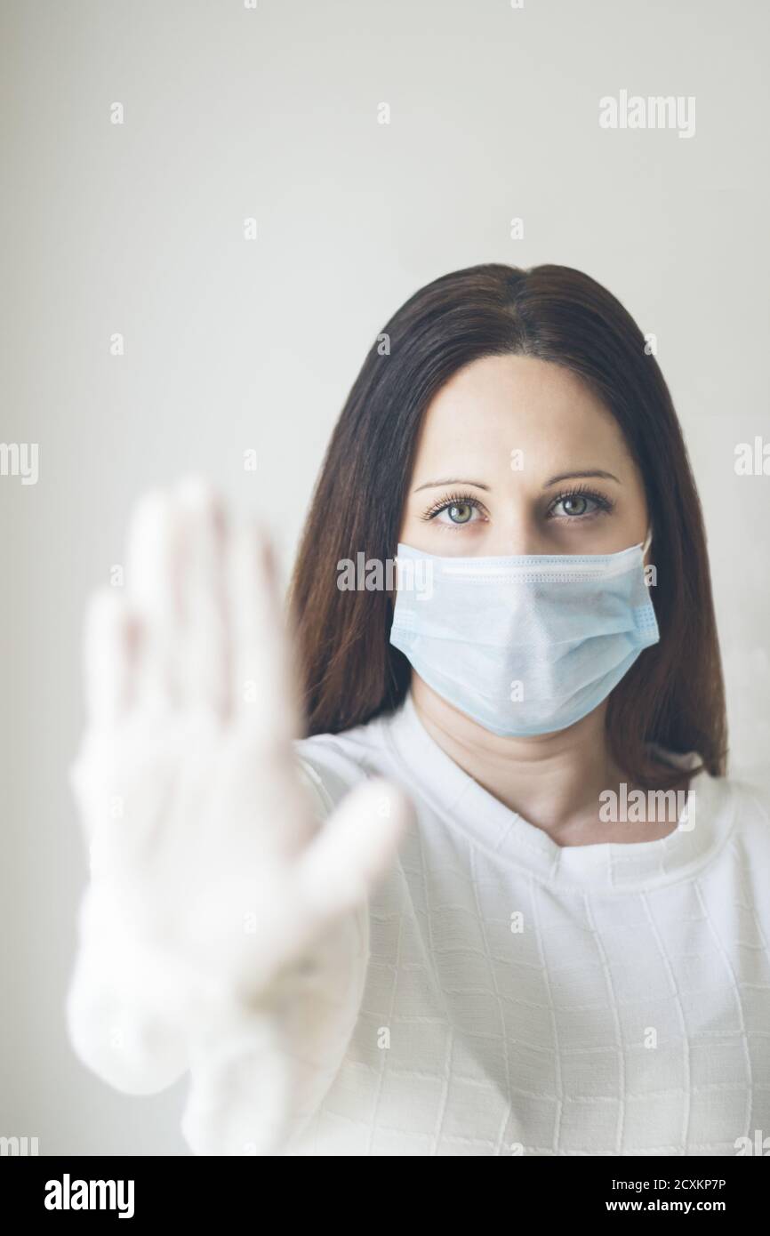 Tir vertical d'une jeune femme portant un masque sanitaire montrant un panneau « top » avec sa main Banque D'Images