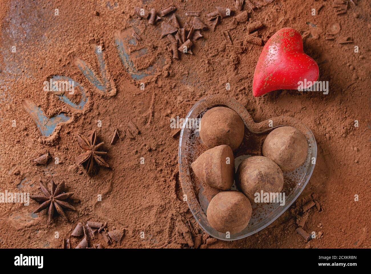 Truffes au chocolat en coeur de verre sur fond en poudre de cacao avec coeurs de Saint-Valentin, étoiles anis et amour lettrage. Vue de dessus. Cadeau pour la Saint-Valentin Banque D'Images