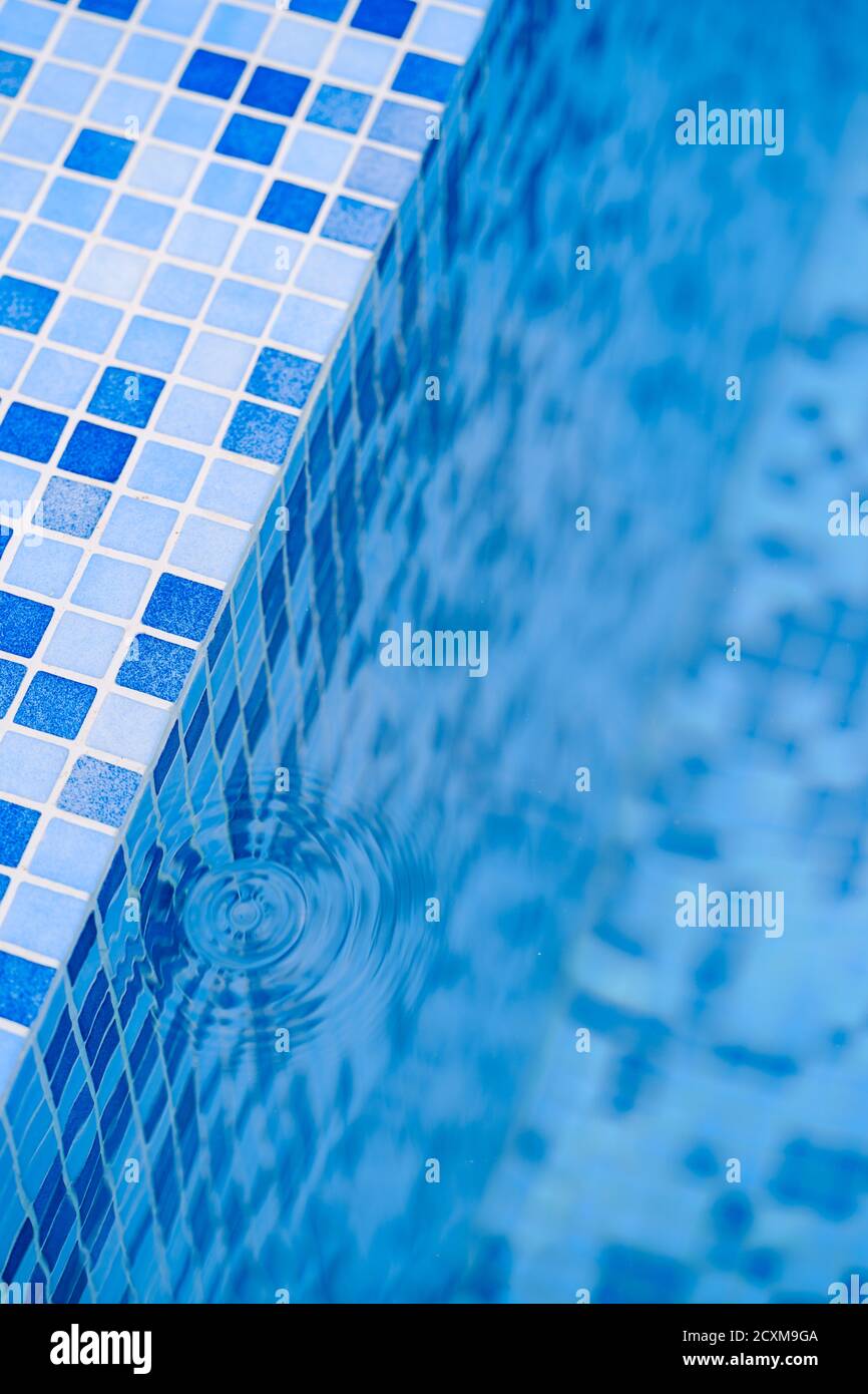 Taches d'eau d'une goutte aux marches avec une mosaïque bleue dans la piscine. Banque D'Images