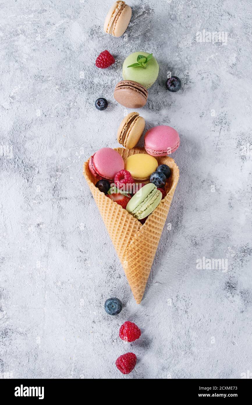 Variété de macarons français doux et colorés au dessert avec différents macarons garnitures servies dans un cornet de gaufres avec de la menthe et des baies fraîches texture sur gris Banque D'Images