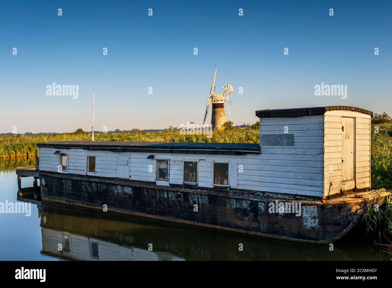 Péniche aménagée sur la rivière Thurne avec le moulin de drainage de niveau de St Benet derrière. Norfolk Broads, Norfolk, Angleterre. Banque D'Images