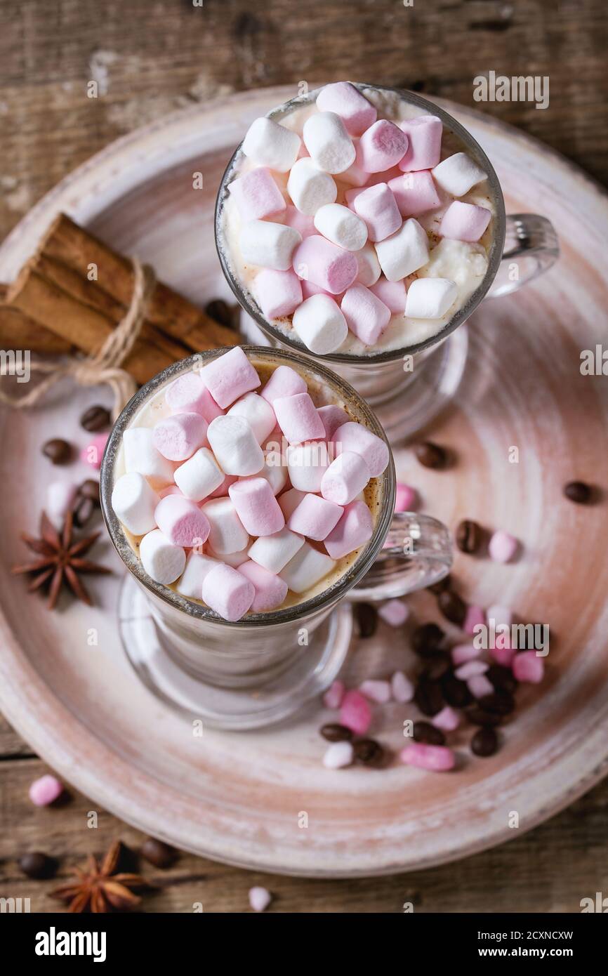 Deux verres de café latte avec guimauve rose debout sur une plaque en céramique avec des épices, les grains de café et sucre rose sur fond de texture en bois. Haut Banque D'Images