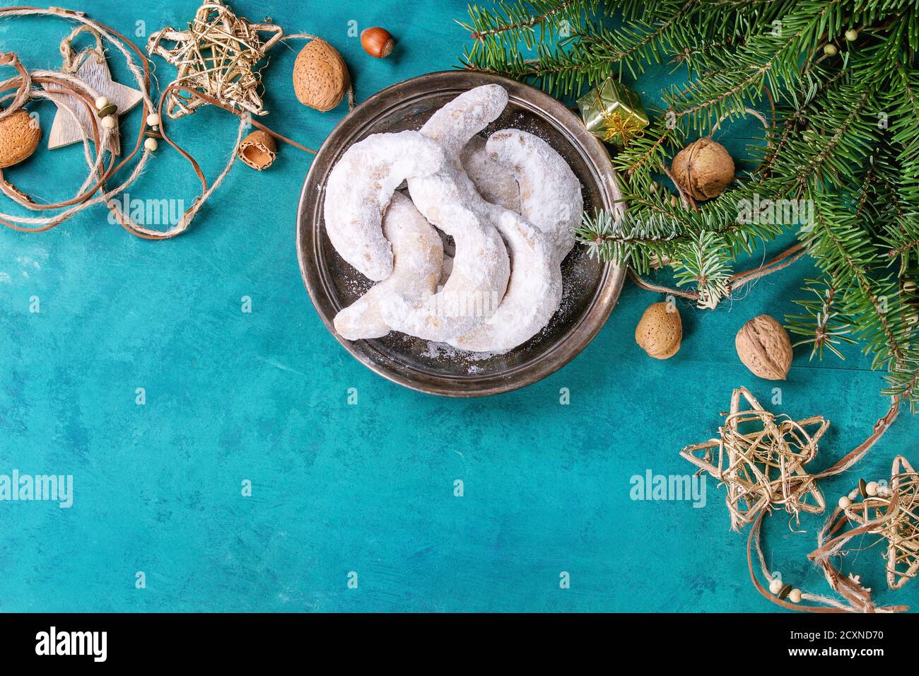 Biscuits aux noix de Noël faits maison croissant de sucre en poudre dans la décoration de vacances et sapin sur la surface de texture en bois turquoise avec espace de copie. Haut Banque D'Images