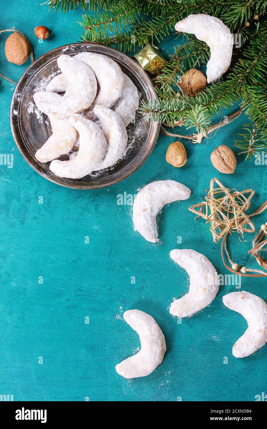 Biscuits aux noix de Noël faits maison croissant de sucre en poudre dans la décoration de vacances et sapin sur la surface de texture en bois turquoise avec espace de copie. Haut Banque D'Images