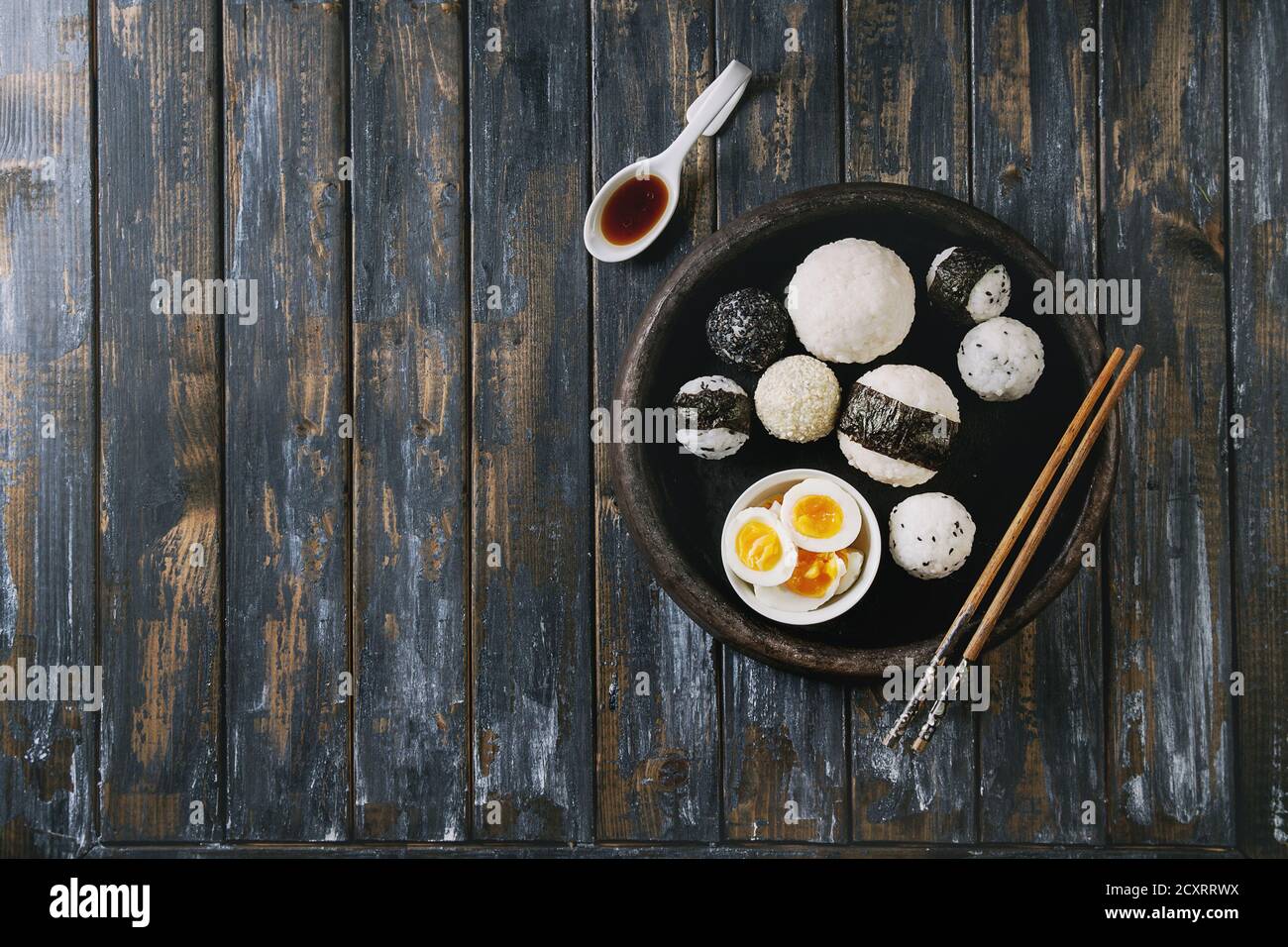 Bac en pierre de taille différente avec des boules de riz et sésame noir Algues Nori, servi avec des œufs durs, de la sauce de soja, baguettes sur planche en bois ba Banque D'Images