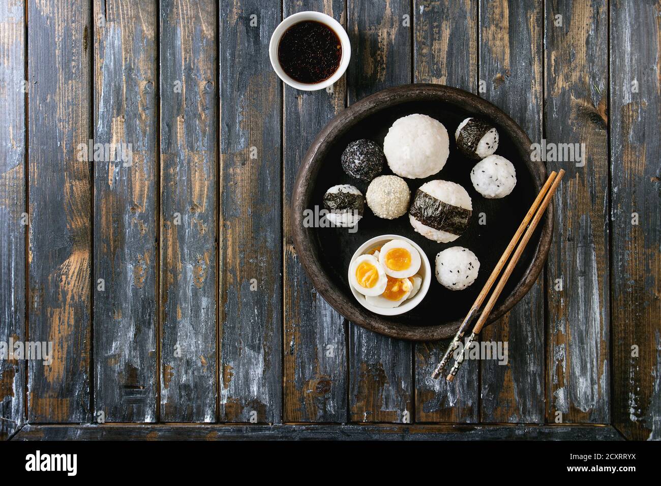 Bac en pierre de taille différente avec des boules de riz et sésame noir Algues Nori, servi avec des œufs durs, de la sauce de soja, baguettes sur planche en bois ba Banque D'Images