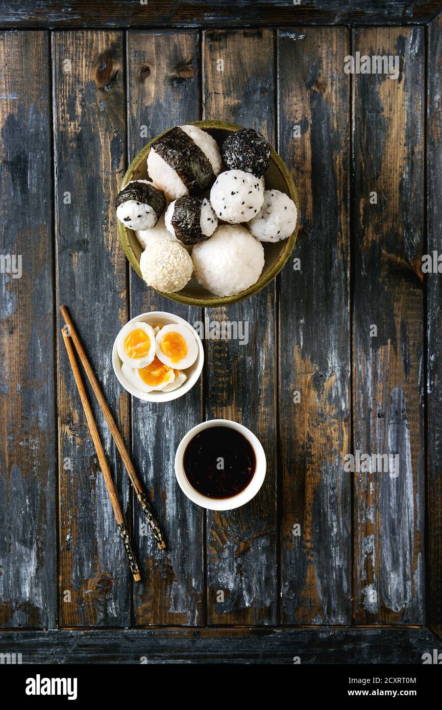 Bac en pierre de taille différente avec des boules de riz et sésame noir Algues Nori, servi avec des œufs durs, de la sauce de soja, baguettes sur planche en bois ba Banque D'Images