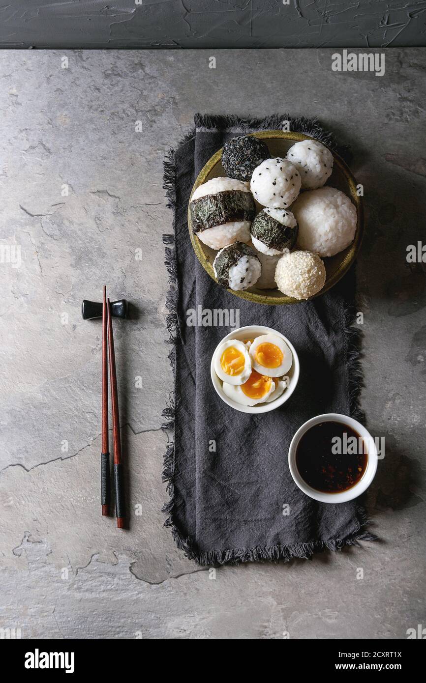 Bol avec différentes tailles de boules de riz et sésame noir avec des Algues Nori, servi avec des œufs durs, de la sauce de soja, des baguettes sur le tableau gris. Asian sty Banque D'Images
