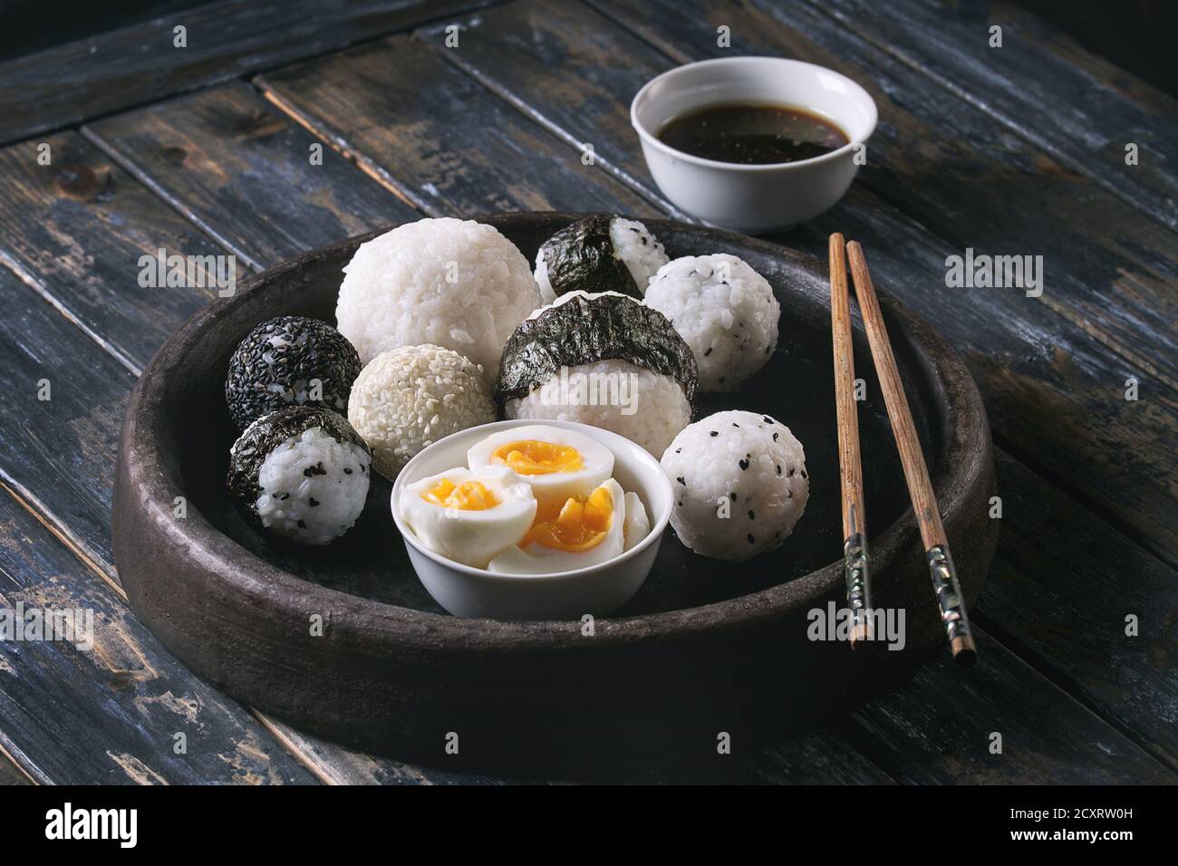Bac en pierre de taille différente avec des boules de riz et sésame noir Algues Nori, servi avec des œufs durs, de la sauce de soja, baguettes sur planche en bois ba Banque D'Images
