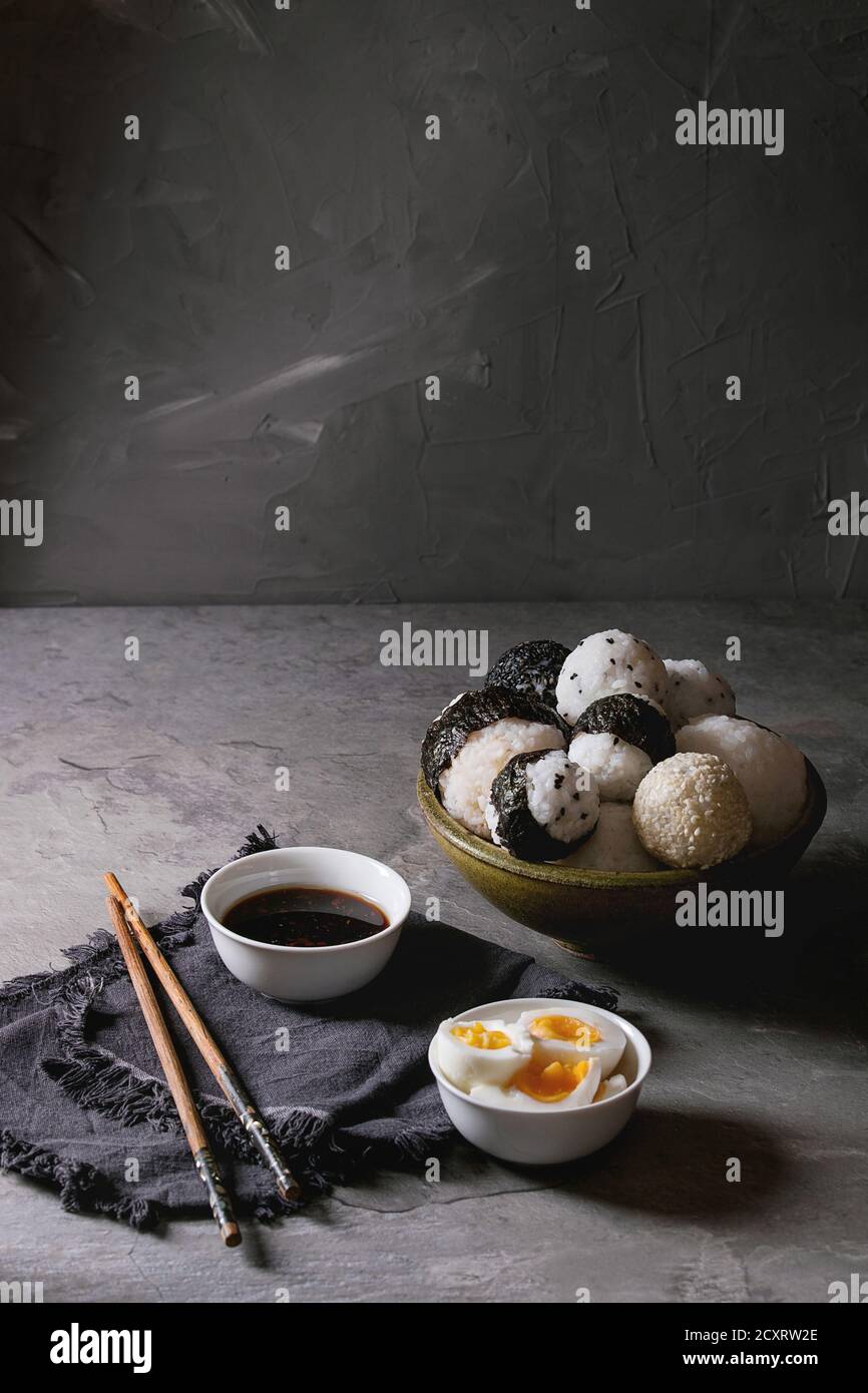 Bol avec différentes tailles de boules de riz et sésame noir avec des Algues Nori, servi avec des œufs durs, de la sauce de soja, des baguettes sur le tableau gris. Asian sty Banque D'Images