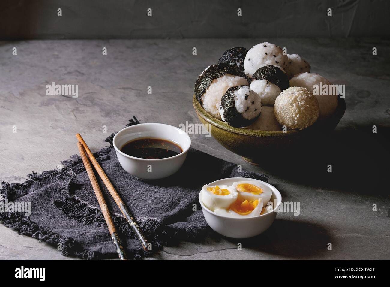 Bol avec différentes tailles de boules de riz et sésame noir avec des Algues Nori, servi avec des œufs durs, de la sauce de soja, des baguettes sur le tableau gris. Asian sty Banque D'Images