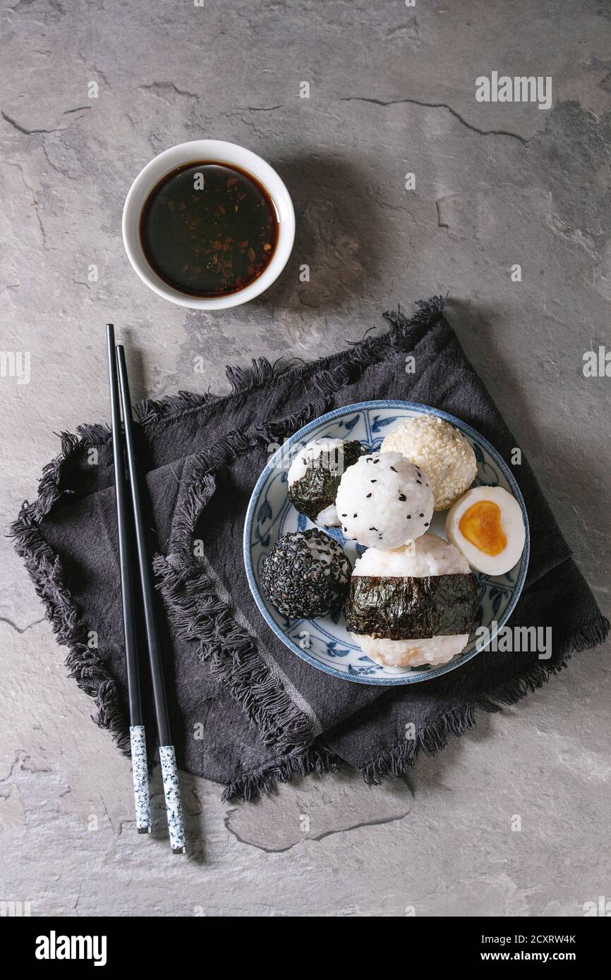 Plaque bleue avec différentes tailles de boules de riz et sésame noir avec des Algues Nori, servi avec des œufs durs, de la sauce de soja, des baguettes sur le tableau gris. Asi Banque D'Images