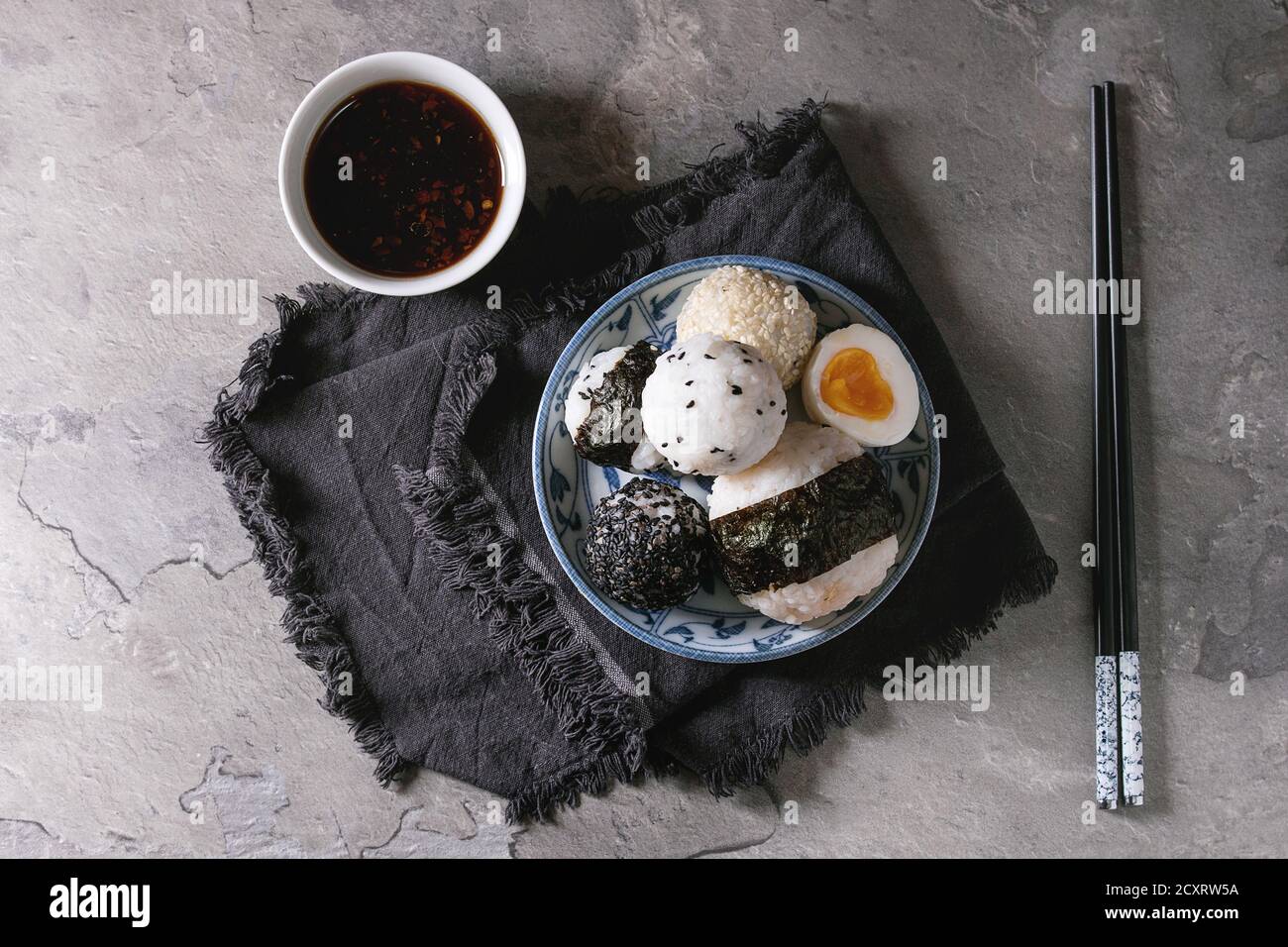 Plaque bleue avec différentes tailles de boules de riz et sésame noir avec des Algues Nori, servi avec des œufs durs, de la sauce de soja, des baguettes sur le tableau gris. Asi Banque D'Images