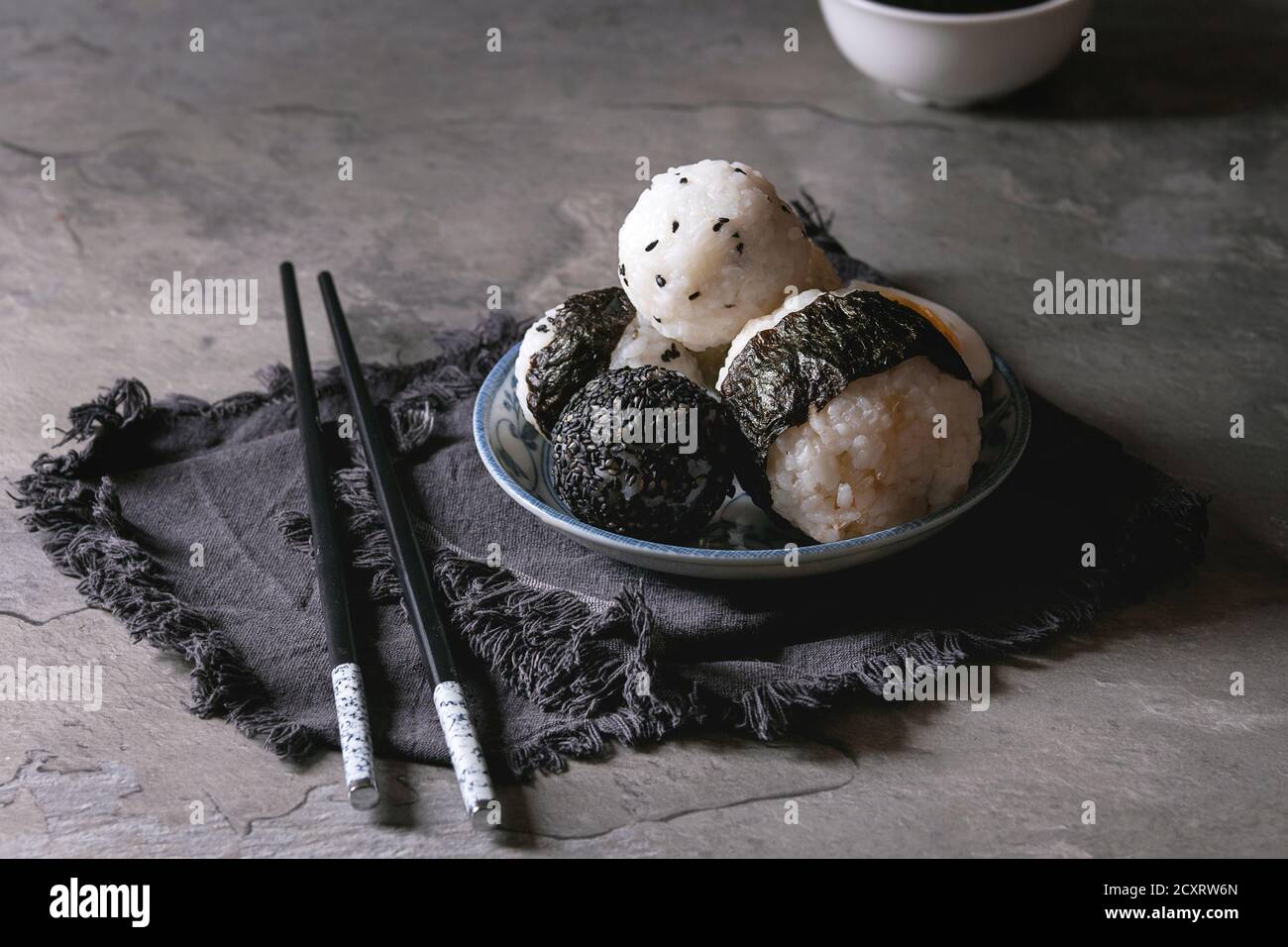 Plaque bleue avec différentes tailles de boules de riz et sésame noir avec des Algues Nori, servi avec des œufs durs, de la sauce de soja, des baguettes sur le tableau gris. Asi Banque D'Images
