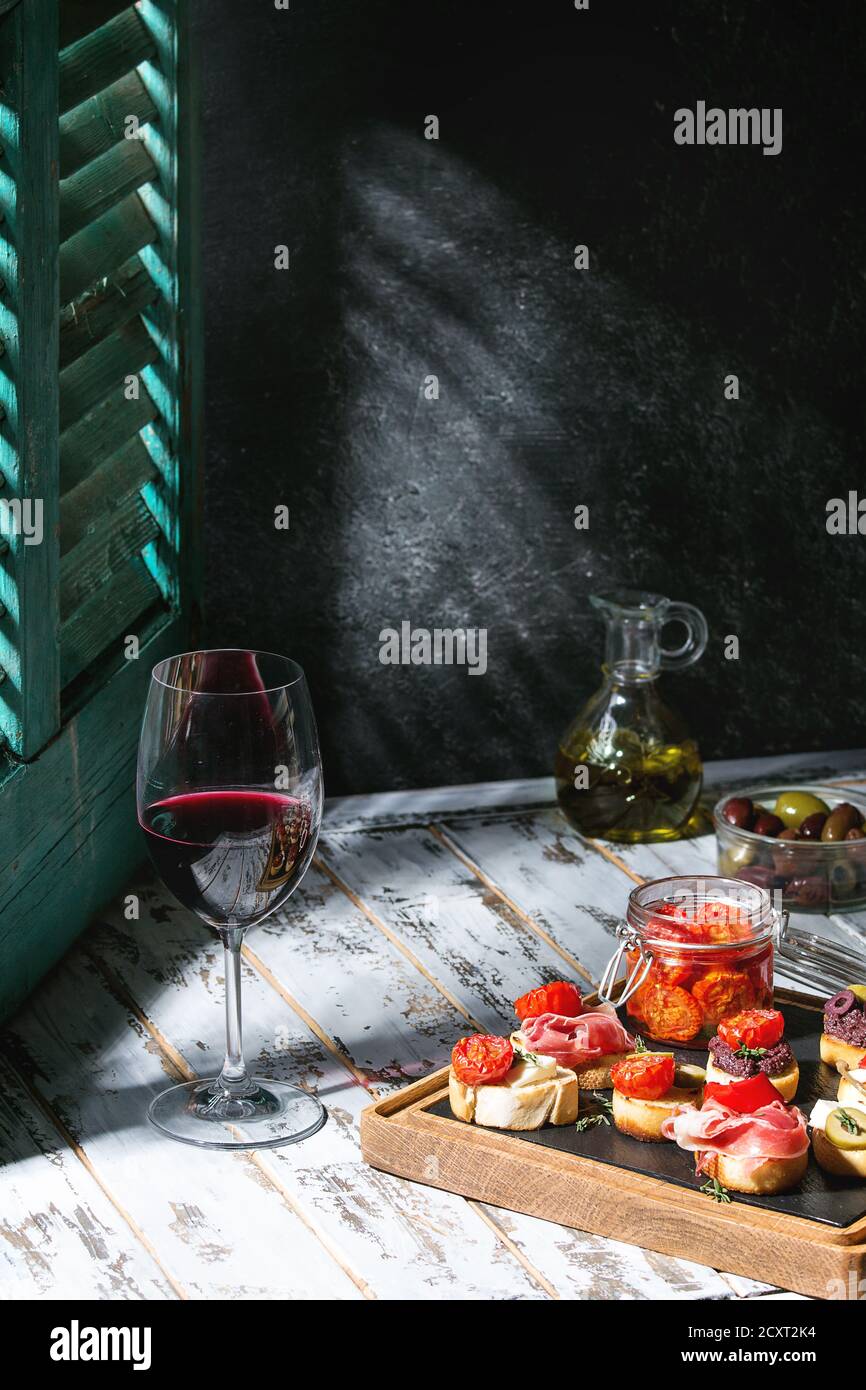 Des tapas ou bruschetta variété. Du pain avec du jambon prosciutto, tomates séchées, huile d'olive, olives, poivre sur ardoise bois board avec verre de vin rouge sur Banque D'Images