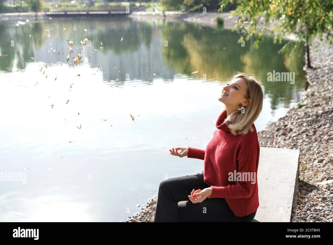 belle jeune femme blonde jette des feuilles vers le haut par le lac et rires. concept d'automne Banque D'Images
