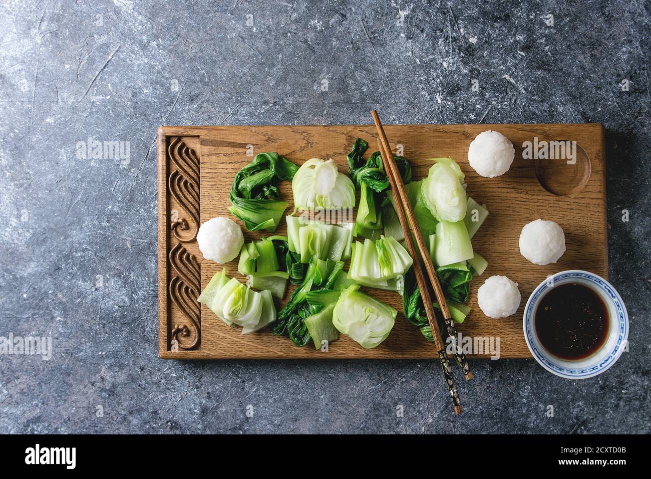 Sauté de bok choy ou chou chinois avec de la sauce soja et de boules de riz servi sur planche à découper en bois décoratif avec des baguettes sur la texture gris backg Banque D'Images