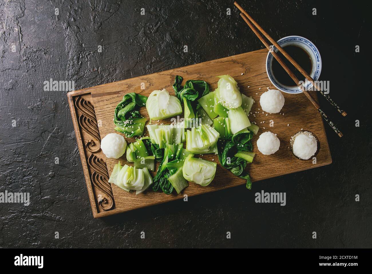 Sauté de bok choy ou chou chinois avec de la sauce soja et de boules de riz servi sur planche à découper en bois décoratif avec des baguettes sur la texture sombre backg Banque D'Images