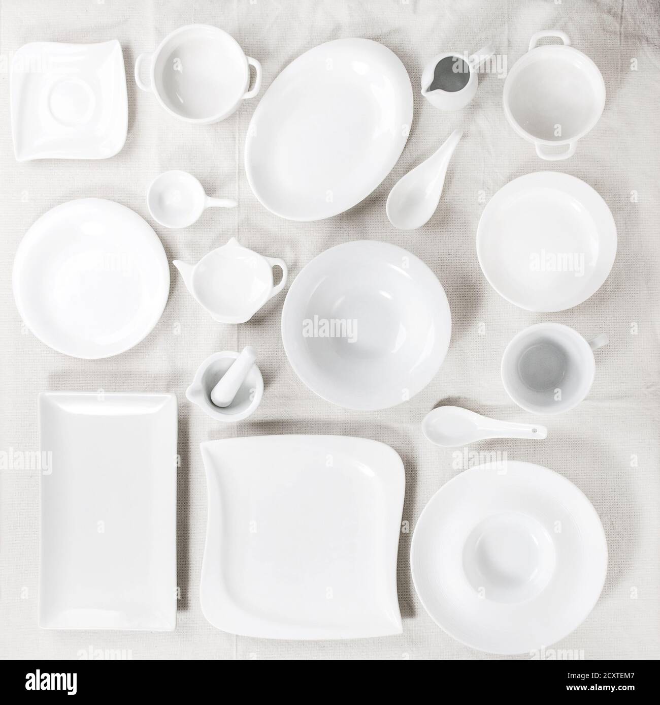 Grand ensemble de assiettes vides en porcelaine blanche et autres vaisselle de différentes tailles et formes par rapport à la nappe blanche en lin. Pose à plat Banque D'Images
