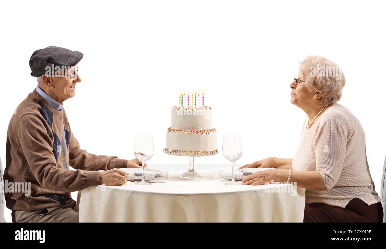 Couple âgé célébrant avec un gâteau d'anniversaire à une table isolé sur fond blanc Banque D'Images