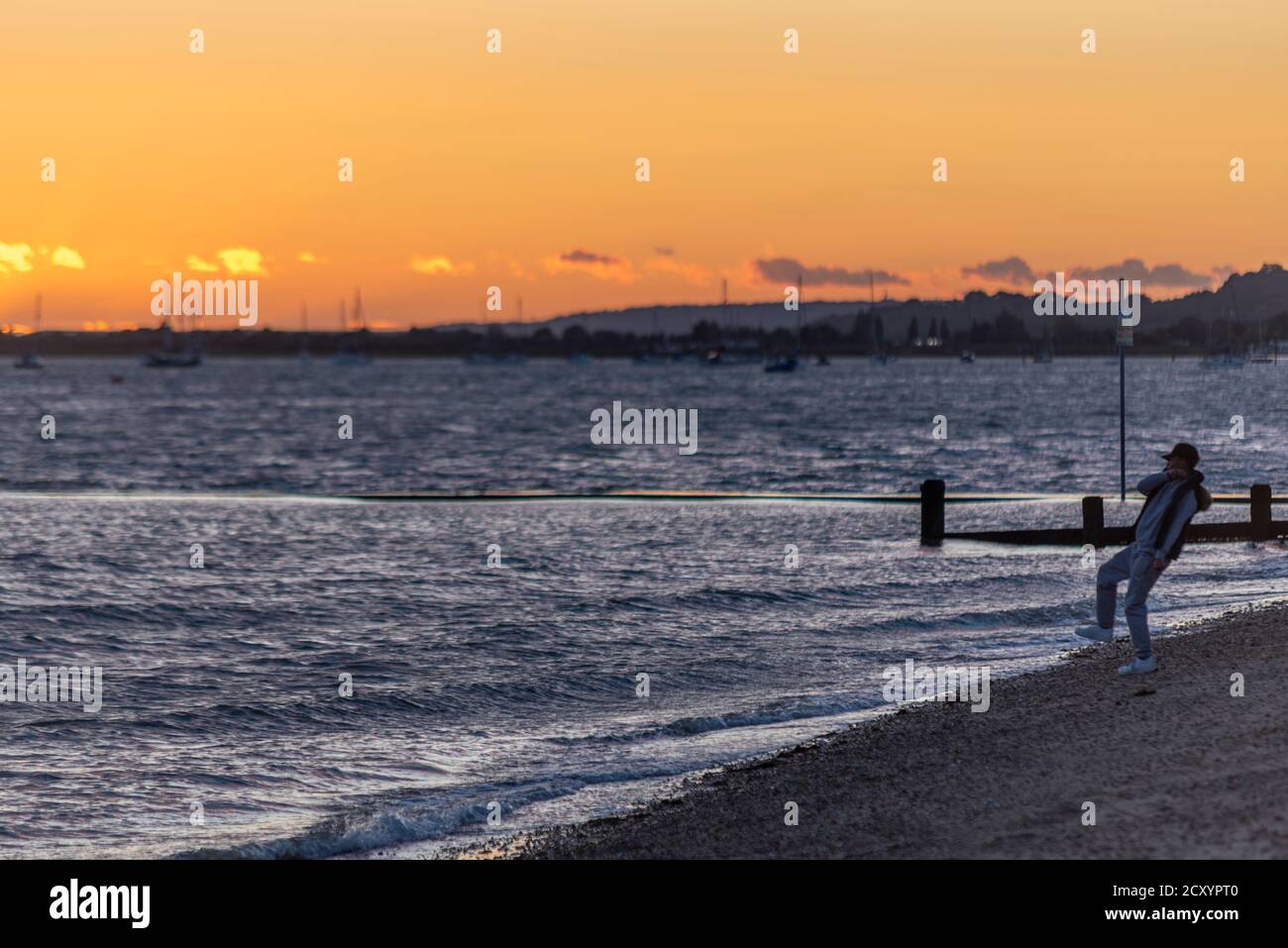 Un homme jette une pierre dans la mer au coucher du soleil à Southend on Sea, Essex, Royaume-Uni. Marée haute de l'estuaire de la Tamise. Homme sur la plage Banque D'Images