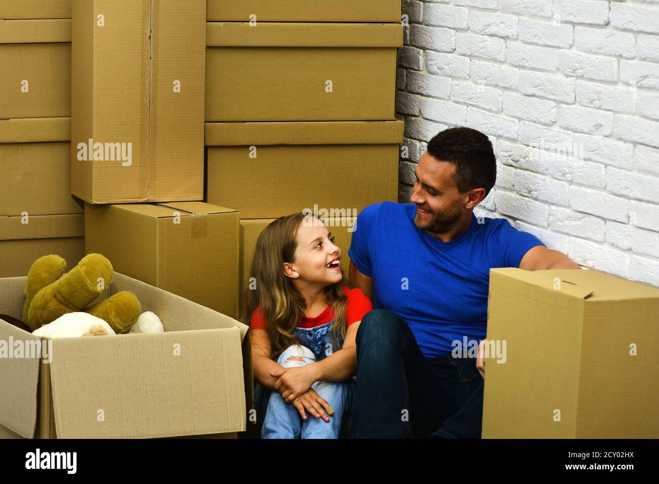 Papa et fille s'assoient par pile de boîtes en carton. Homme et fille près  de la boîte avec des jouets sur fond de mur de brique blanche. Nouveau  concept de maison et