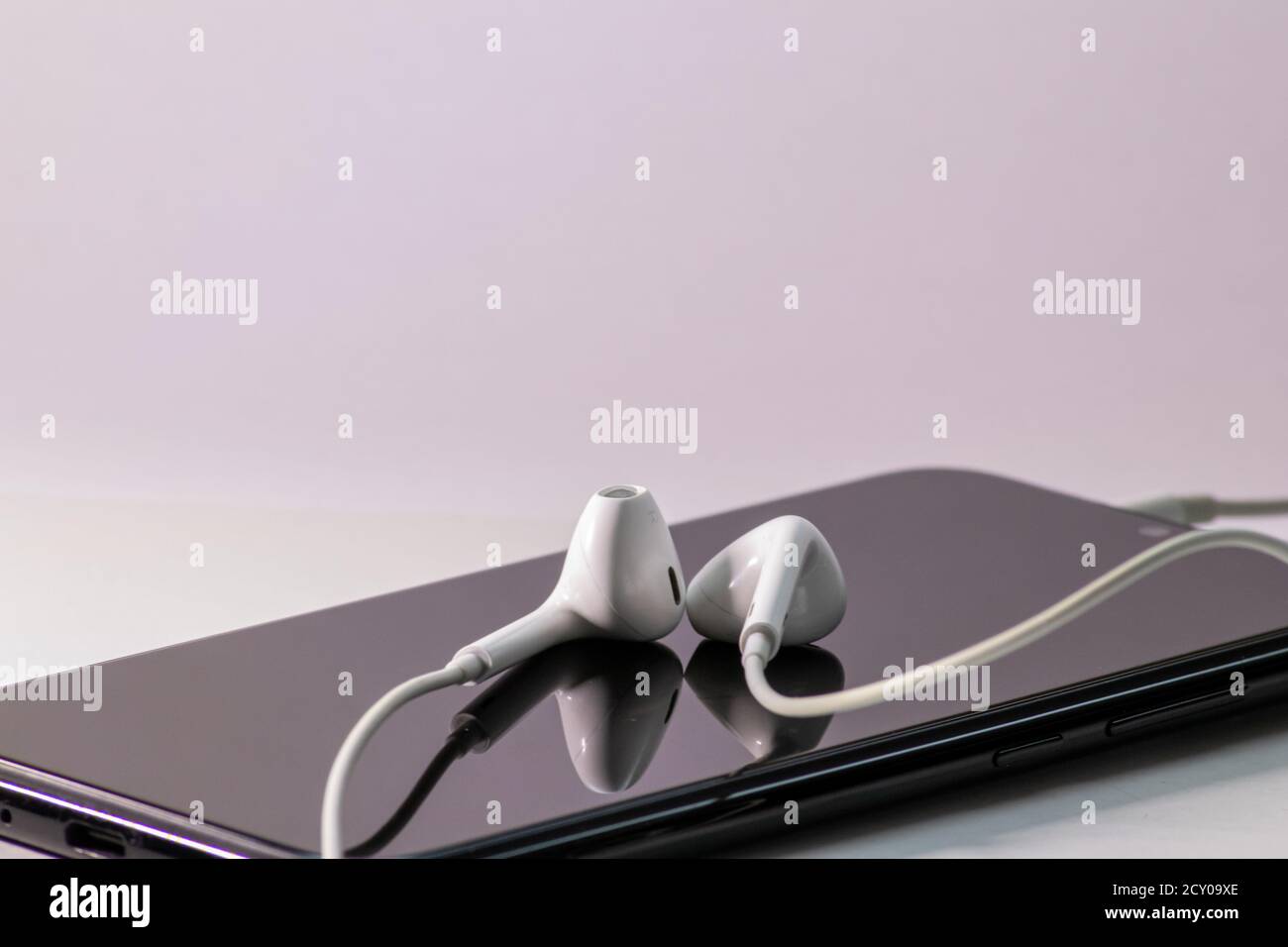 Smartphone noir en tant que périphérique mobile pour la diffusion de vidéos et la diffusion en continu audio ou écouter des flux audio et vidéo à emporter avec écouteurs intra-auriculaires blancs Banque D'Images