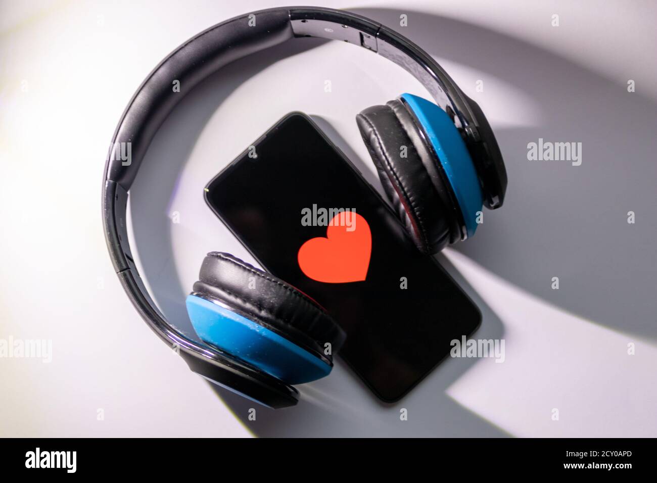 Un smartphone noir avec cœur rouge sur l'écran noir et un casque circum-aural sans fil bleu vous permet d'écouter de la musique en streaming, de contrôler votre état de santé et de profiter d'un smartphone Banque D'Images