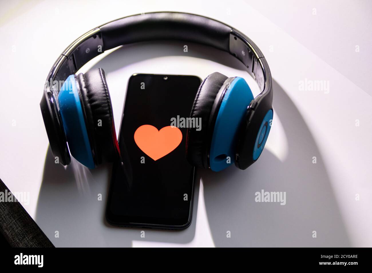 Un smartphone noir avec cœur rouge sur l'écran noir et un casque circum-aural sans fil bleu vous permet d'écouter de la musique en streaming, de contrôler votre état de santé et de profiter d'un smartphone Banque D'Images