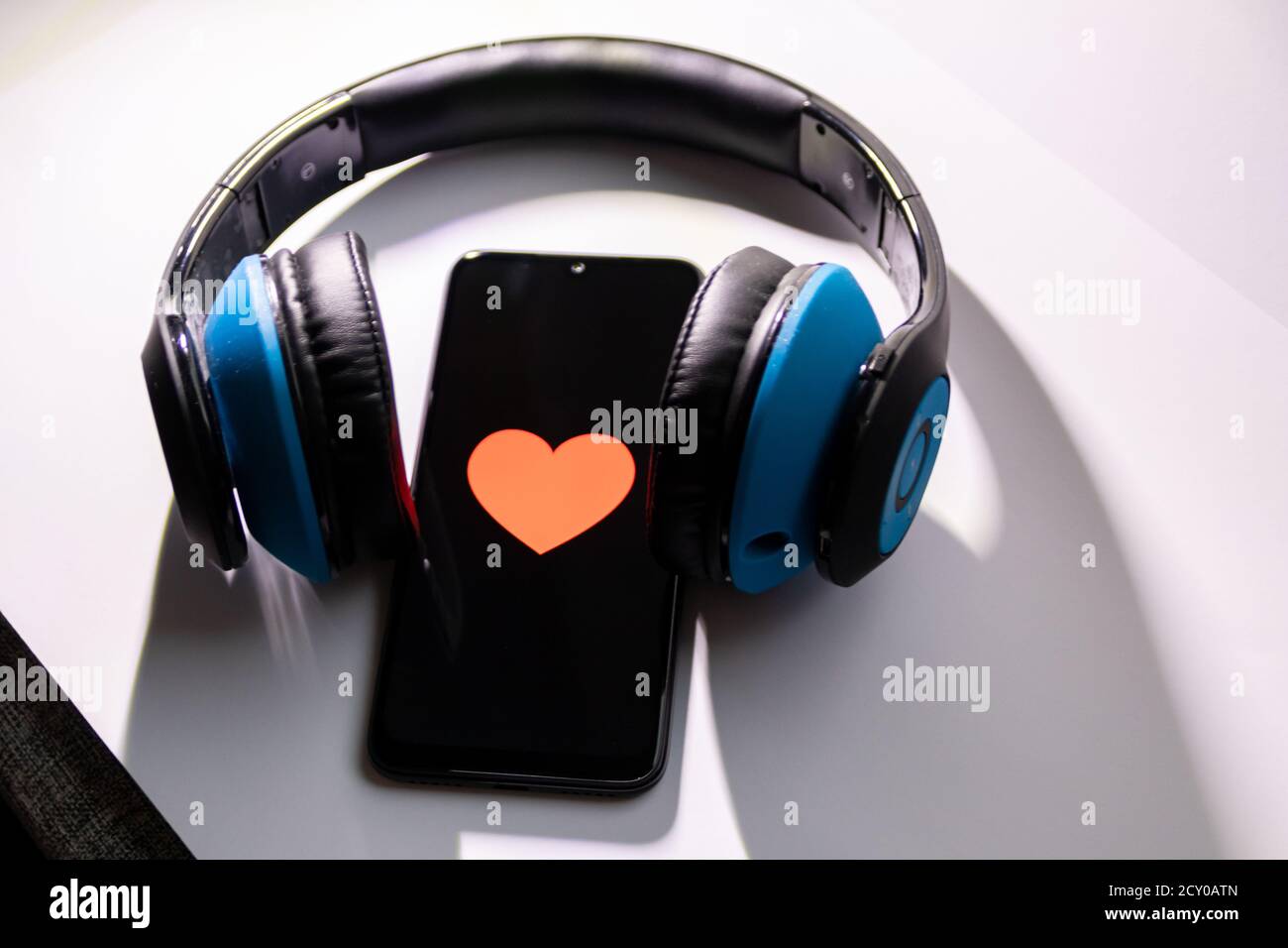 Un smartphone noir avec cœur rouge sur l'écran noir et un casque circum-aural sans fil bleu vous permet d'écouter de la musique en streaming, de contrôler votre état de santé et de profiter d'un smartphone Banque D'Images