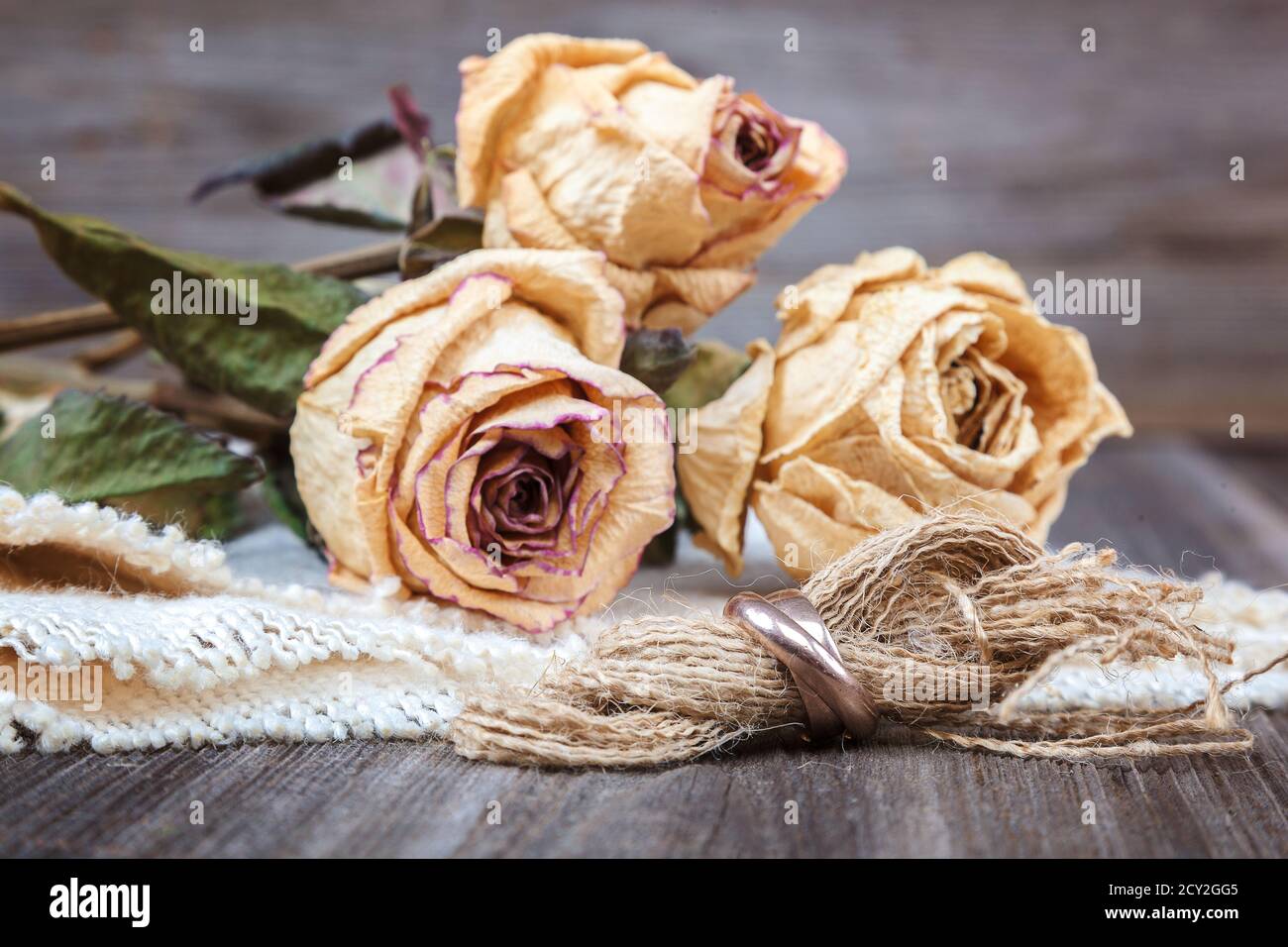 Anneaux de mariage et roses fleurs séchées sur fond de bois. Banque D'Images
