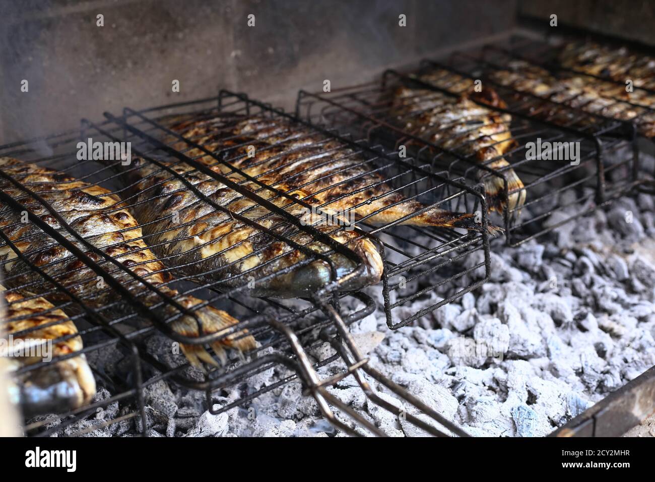 Le processus de cuisson du poisson dorado sur le barbecue au feu. Fruits de mer méditerranéens grillés sur fond de briques Banque D'Images