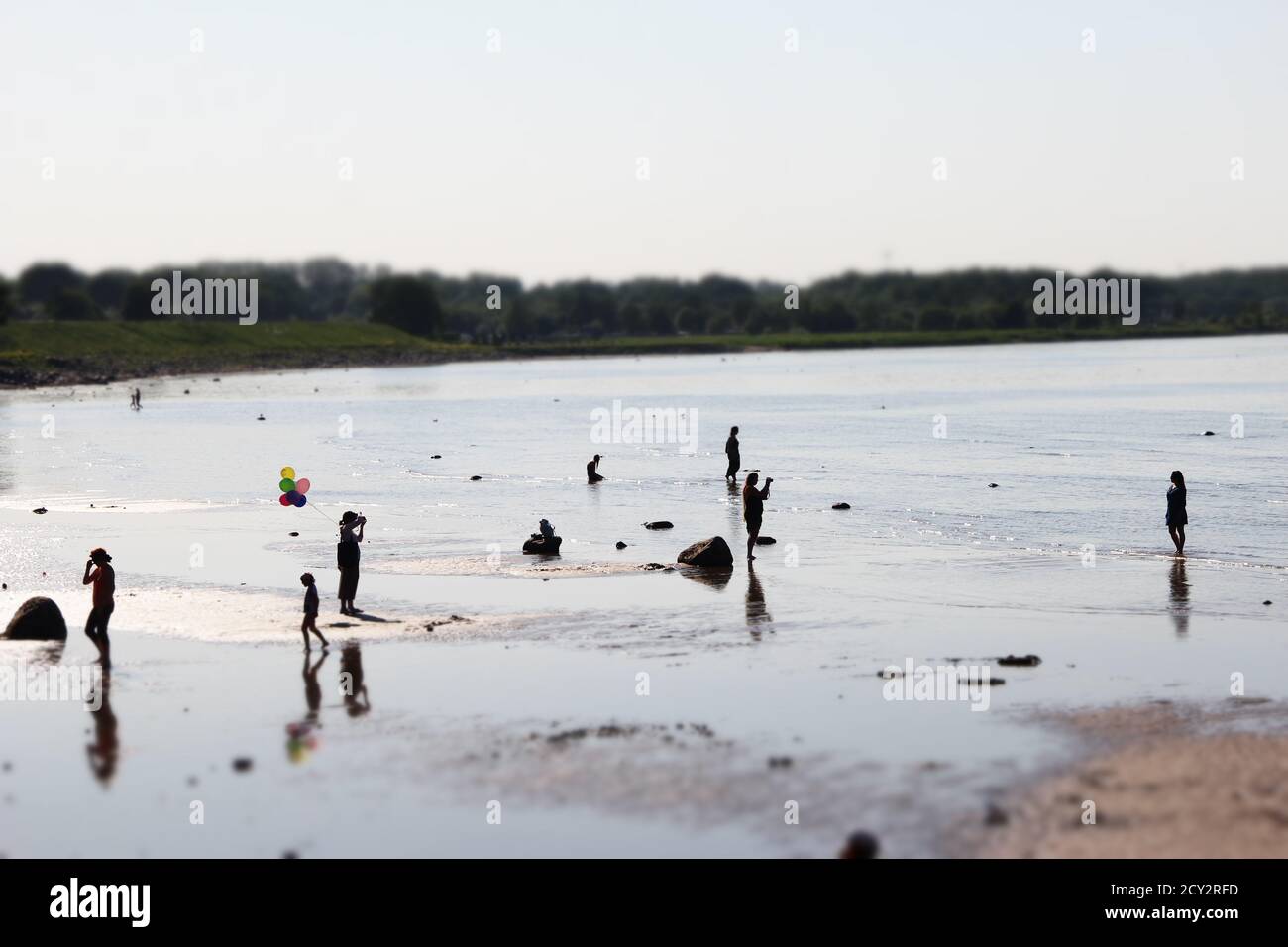 les gens qui marchent debout et se baignent à la plage. Une personne avec des ballons colorés et une forêt en arrière-plan Banque D'Images