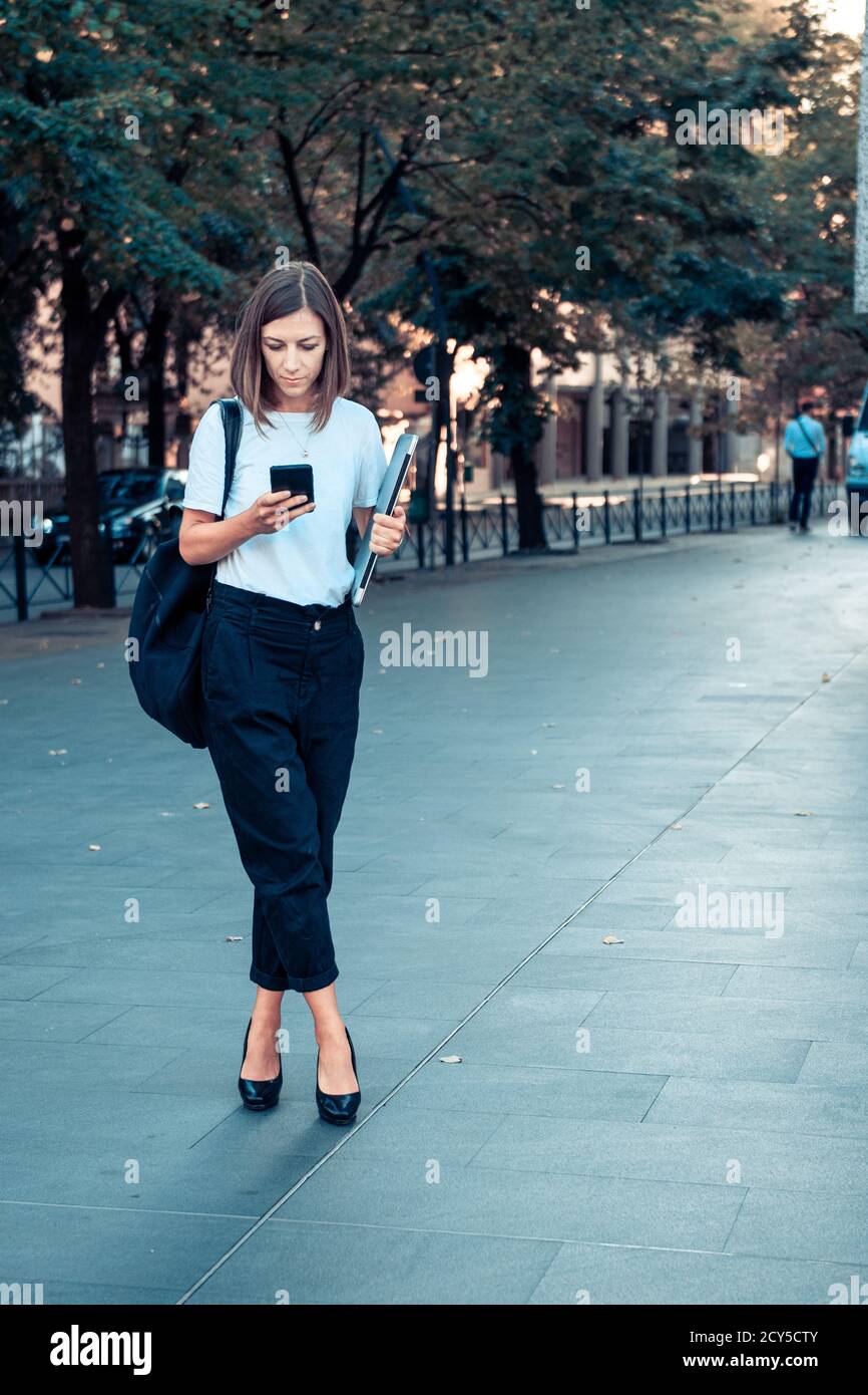 Femme d'affaires avec ordinateur portable et smartphone dans la rue. Banque D'Images