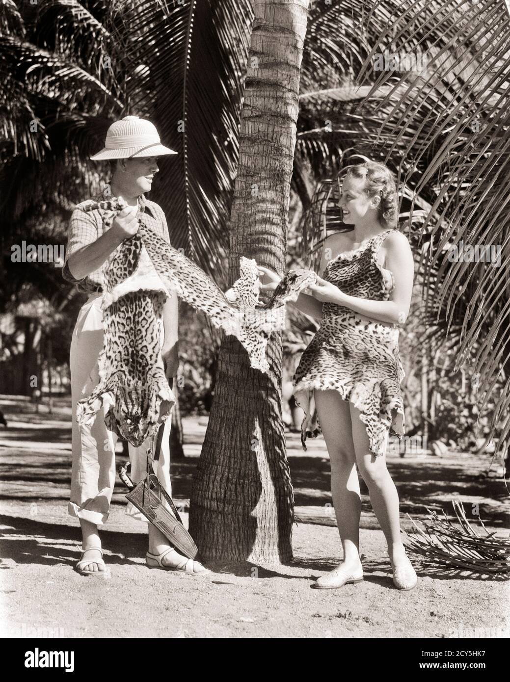 HOMME DES ANNÉES 1930 GRAND BLANC HUNTER TYPE ET FEMME JUNGLE HUNTRESS PORTER DES PEAUX DE LÉOPARD PARLANT SOUS LE PALMIER TENANT DES PEAUX DE FOURRURE - R9926 HAR001 HARS STYLE DE VIE JUNGLE ACTEUR FEMMES COPIE ESPACE AMITIÉ FEMMES HOMMES HUNTER DIVERTISSEMENT PEAU B&W FILMS BIZARRE FILMS AVENTURE CINÉMAS INTERPRÈTE ÉTRANGE GROTESQUE PITH ZANY NON CONVENTIONNEL ENTERTAINER OCCUPATIONS ACTEURS PELT PELT PTS STYLE WACKY IDIOSYNCRATIQUE MOTION PICTURE MOTION PICTURES TRADE AMUSE COOPERATION ARTISTES EXCENTRIQUES HUNTRESS HOMME MI-ADULTE HOMME MI-ADULTE FEMME MI-ADULTE INTERPRÈTE PEAU DE CASQUE Banque D'Images